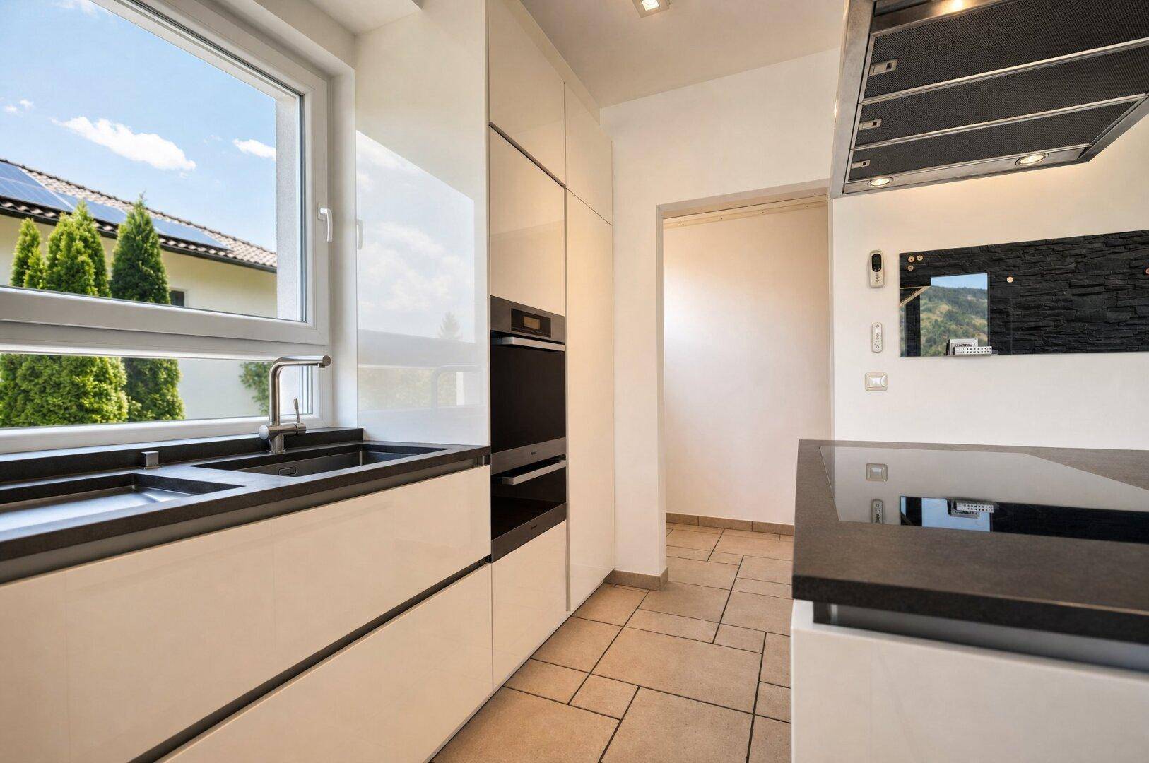 Funktionale Küche mit weißen Hochglanzschränken, dunkler Arbeitsplatte und Fenster mit Blick nach draußen.