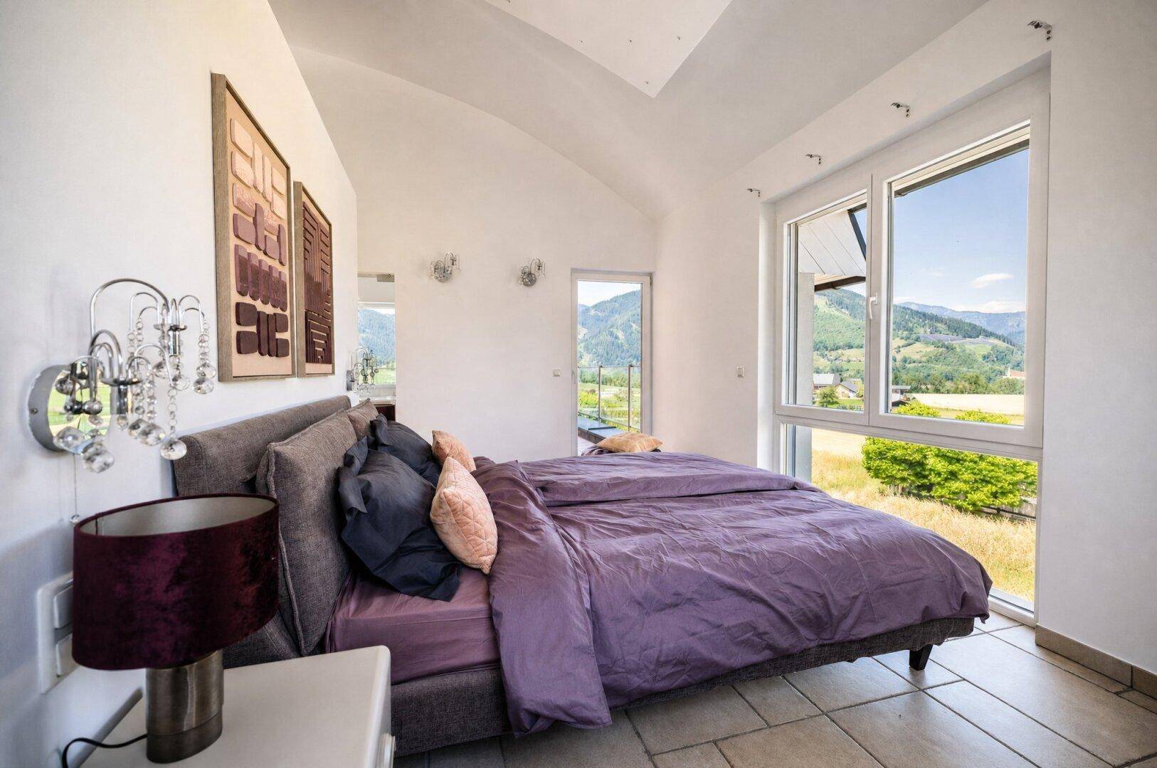 Schlafzimmer mit schrägen Decken, großem Bett und bodentiefen Fenstern mit weitem Bergblick.
