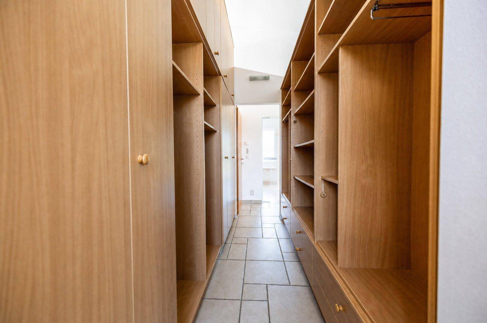 Geräumiger begehbarer Kleiderschrank mit vielen Holzregalen und Stauraum.