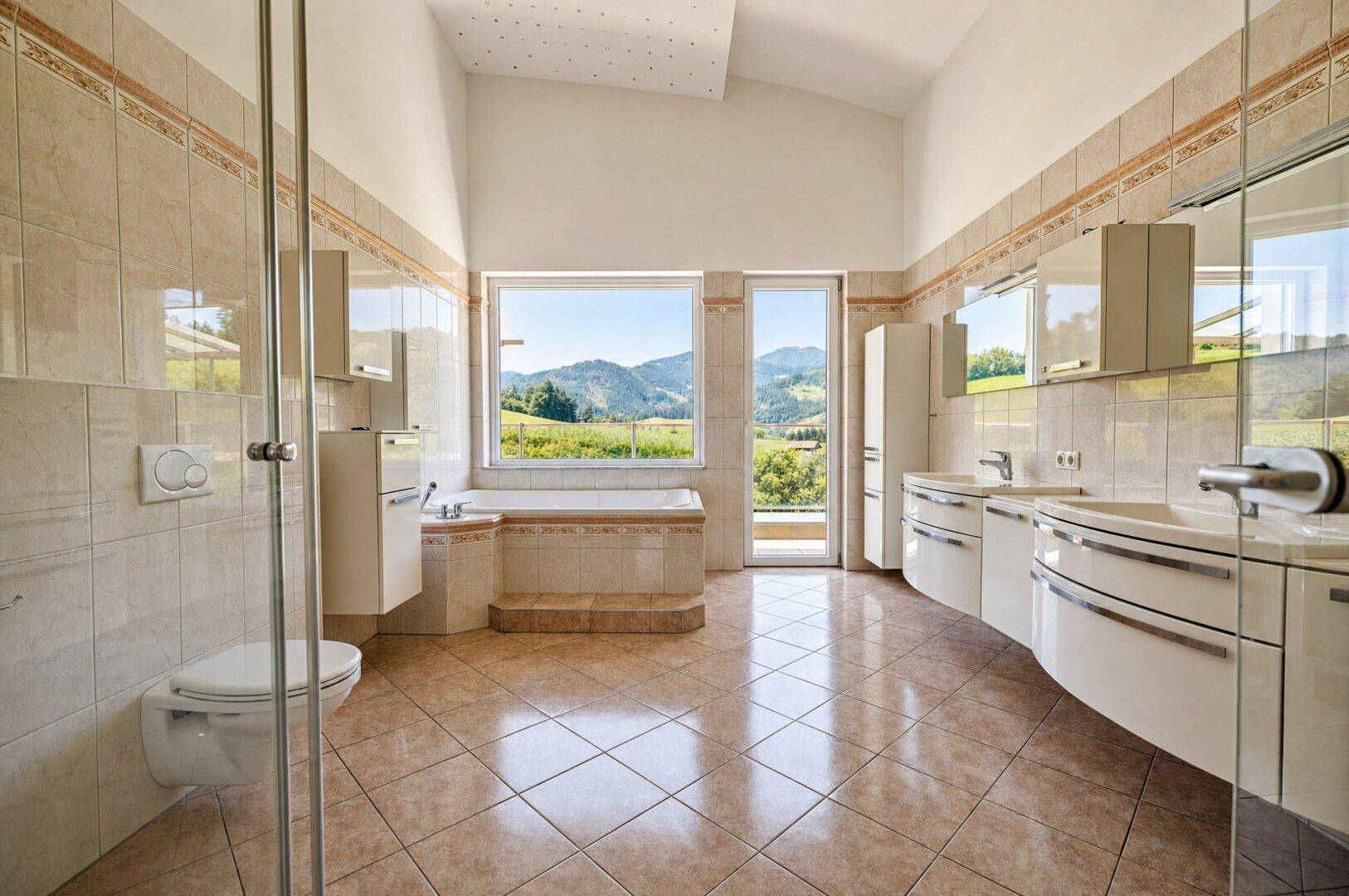 Großes Badezimmer mit Badewanne, Doppelwaschbecken und weitem Blick auf die grüne Landschaft.
