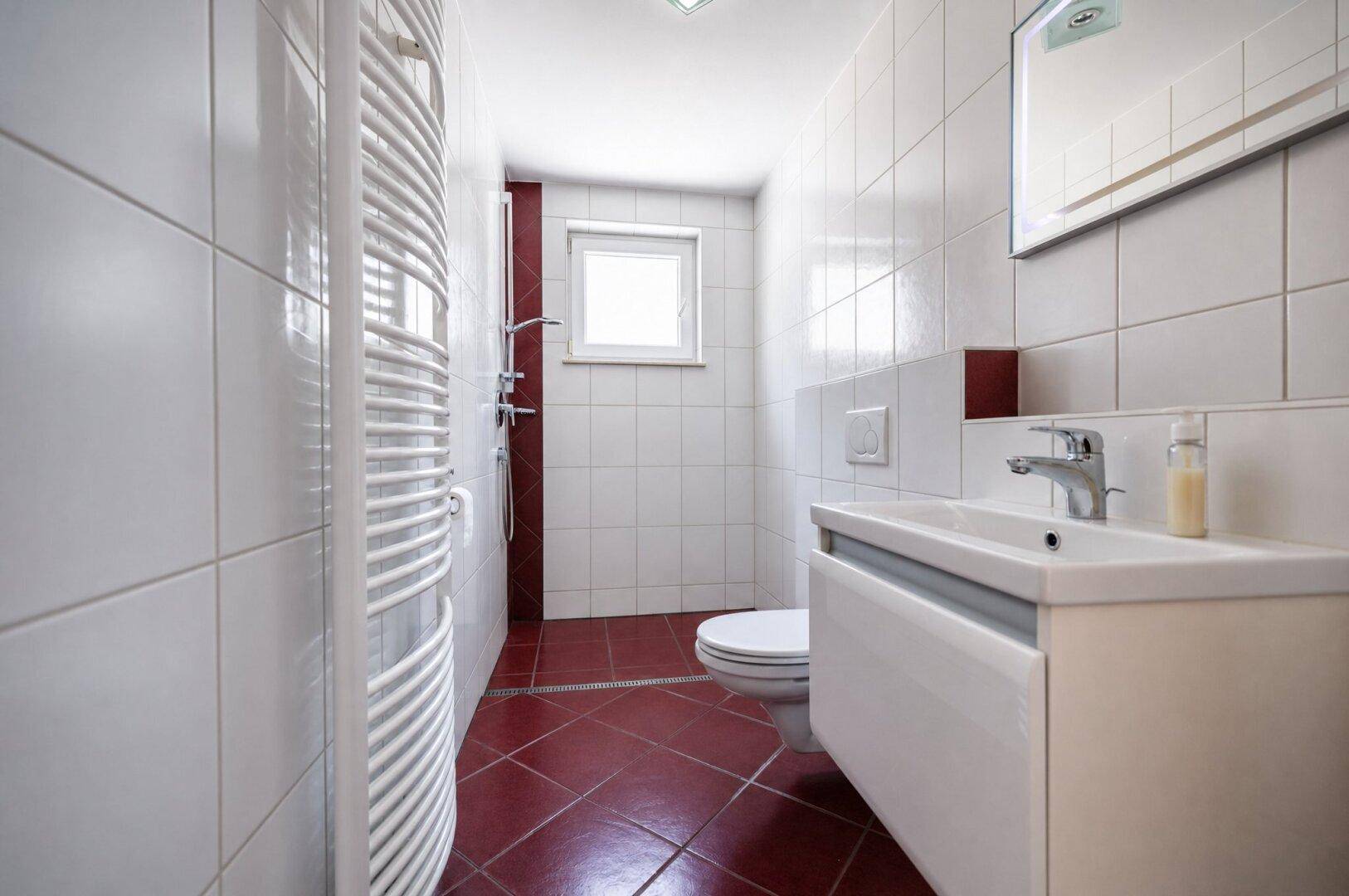 Modernes Badezimmer mit weißen Fliesen, Dusche, WC und beheiztem Handtuchhalter.