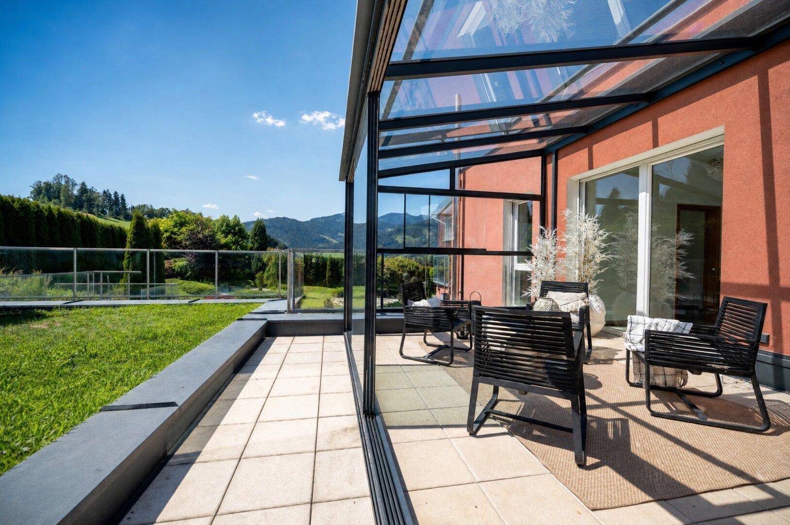 Überdachte Terrasse mit modernen Gartenmöbeln und weitem Blick auf die grüne Landschaft.