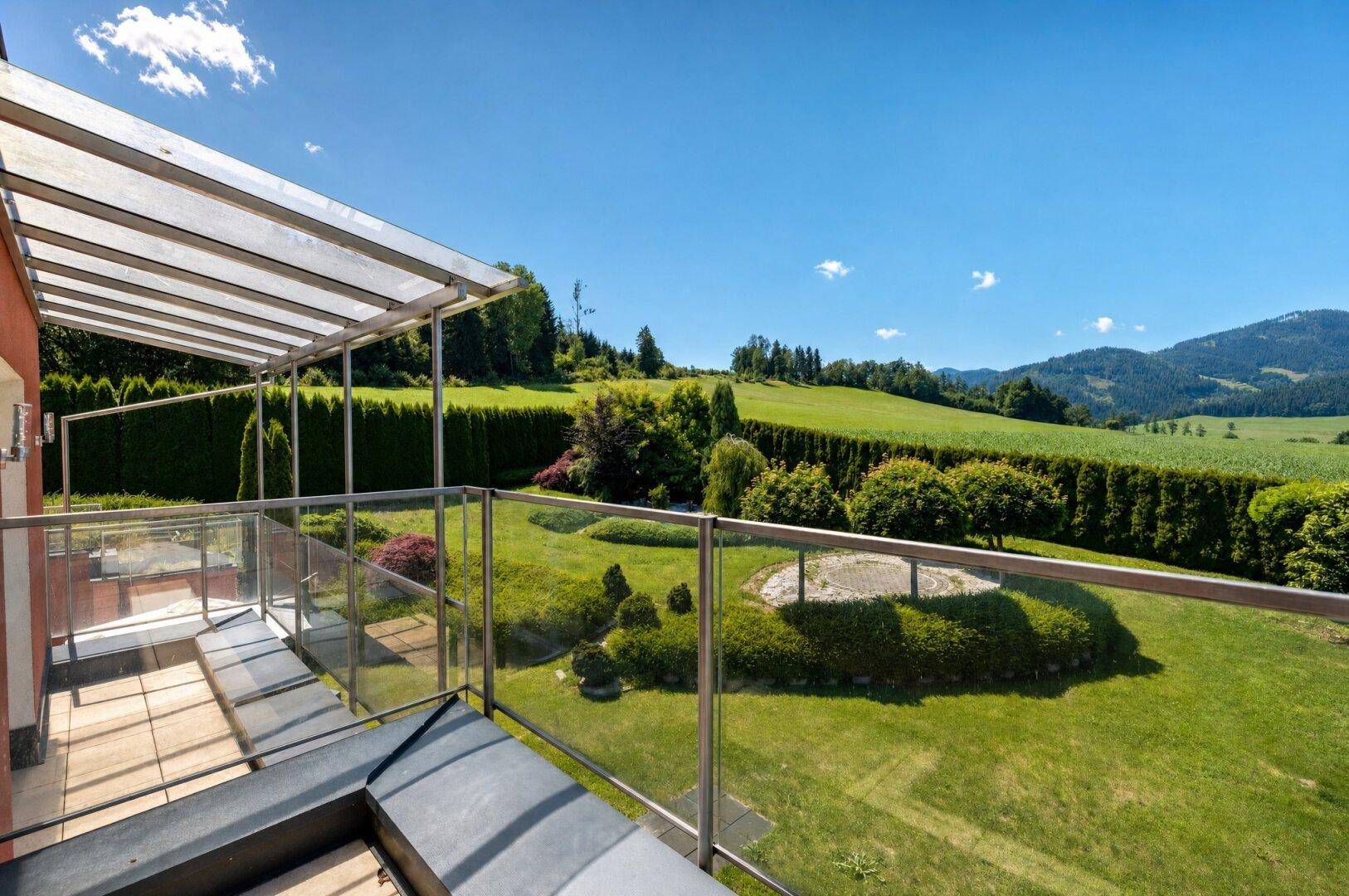 Großer Balkon mit Glasgeländer und Panoramablick auf die umliegende grüne Hügellandschaft.