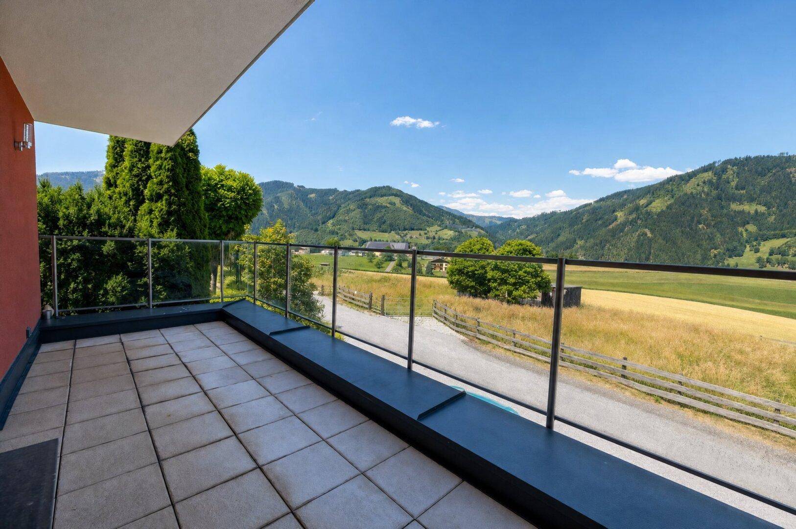 Geräumiger Balkon mit Fliesenboden und Glasgeländer bietet einen weiten Blick auf die umliegende Berglandschaft.