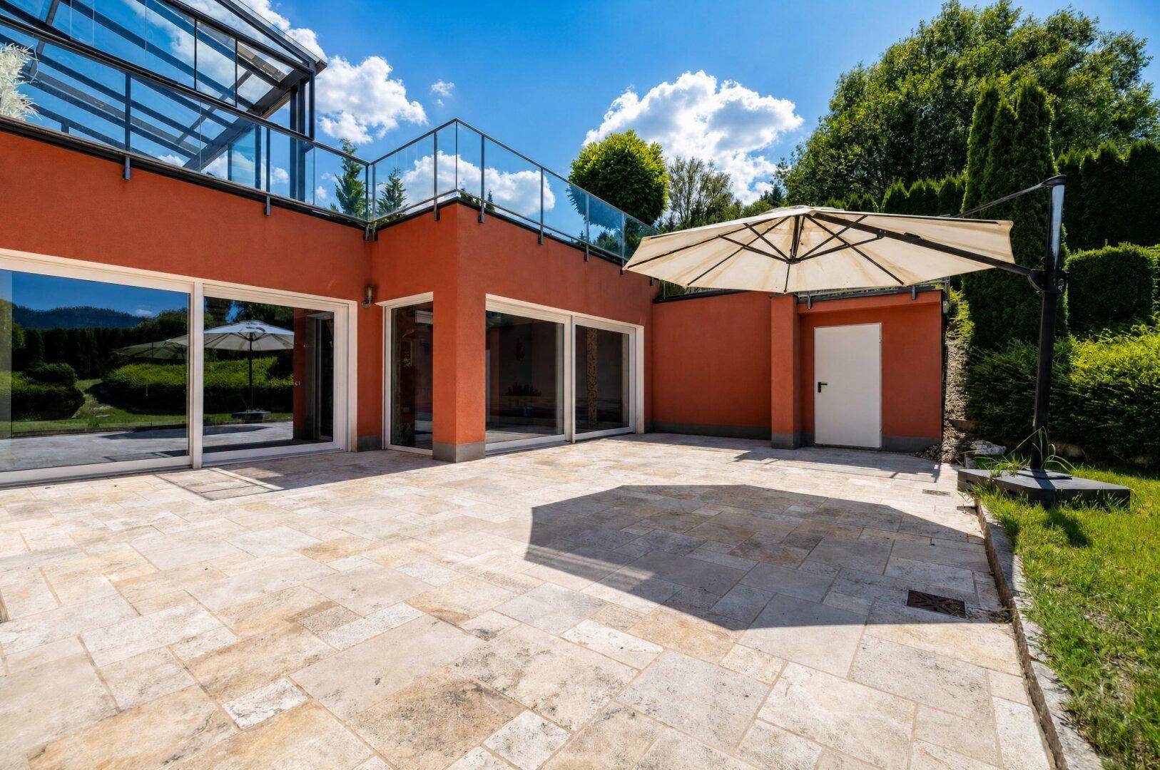 Weitläufige Terrasse mit hellen Steinplatten und großen Glasfronten, die zum Garten hin öffnen.