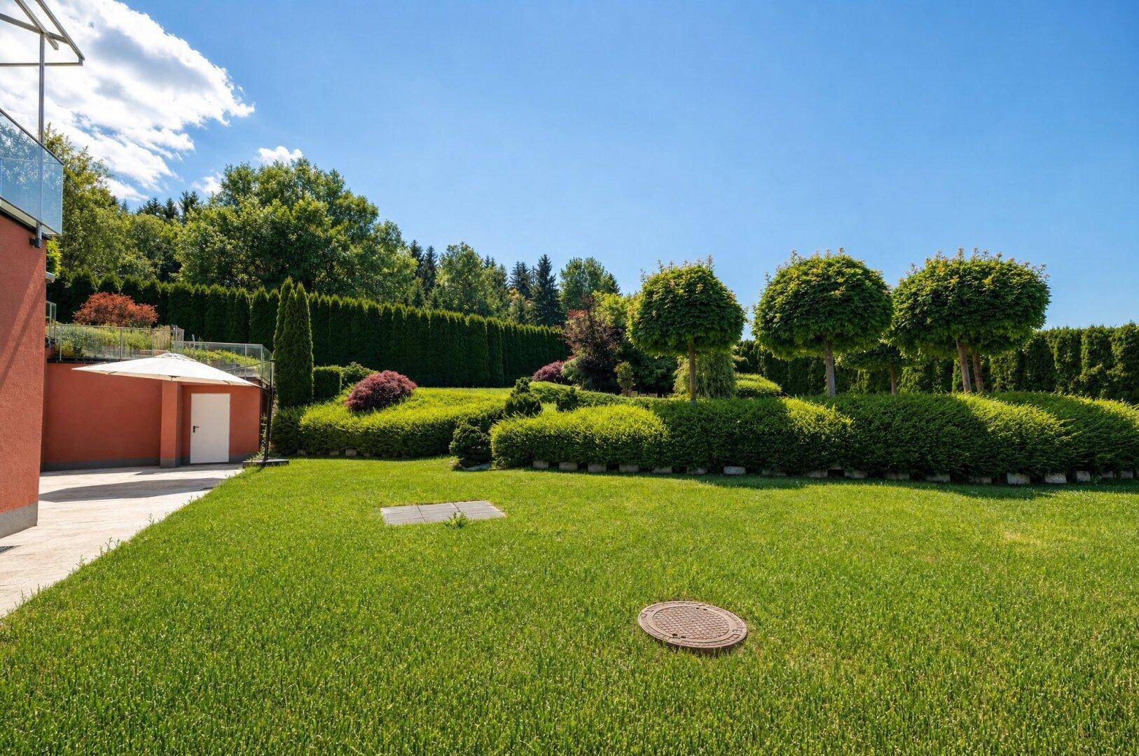 Attraktiver Garten mit akkurat geschnittenen Hecken, Rasenflächen und dekorativen Bäumen neben dem Haus.