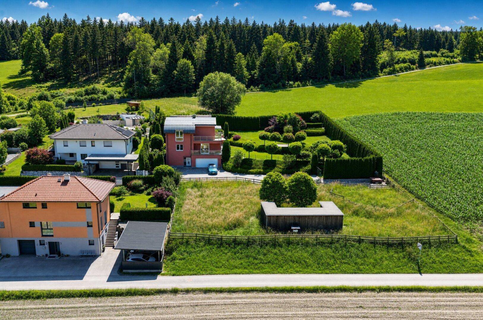 Luftaufnahme des Anwesens mit modernem Haus, gepflegtem Garten und angrenzenden Feldern und Wald.