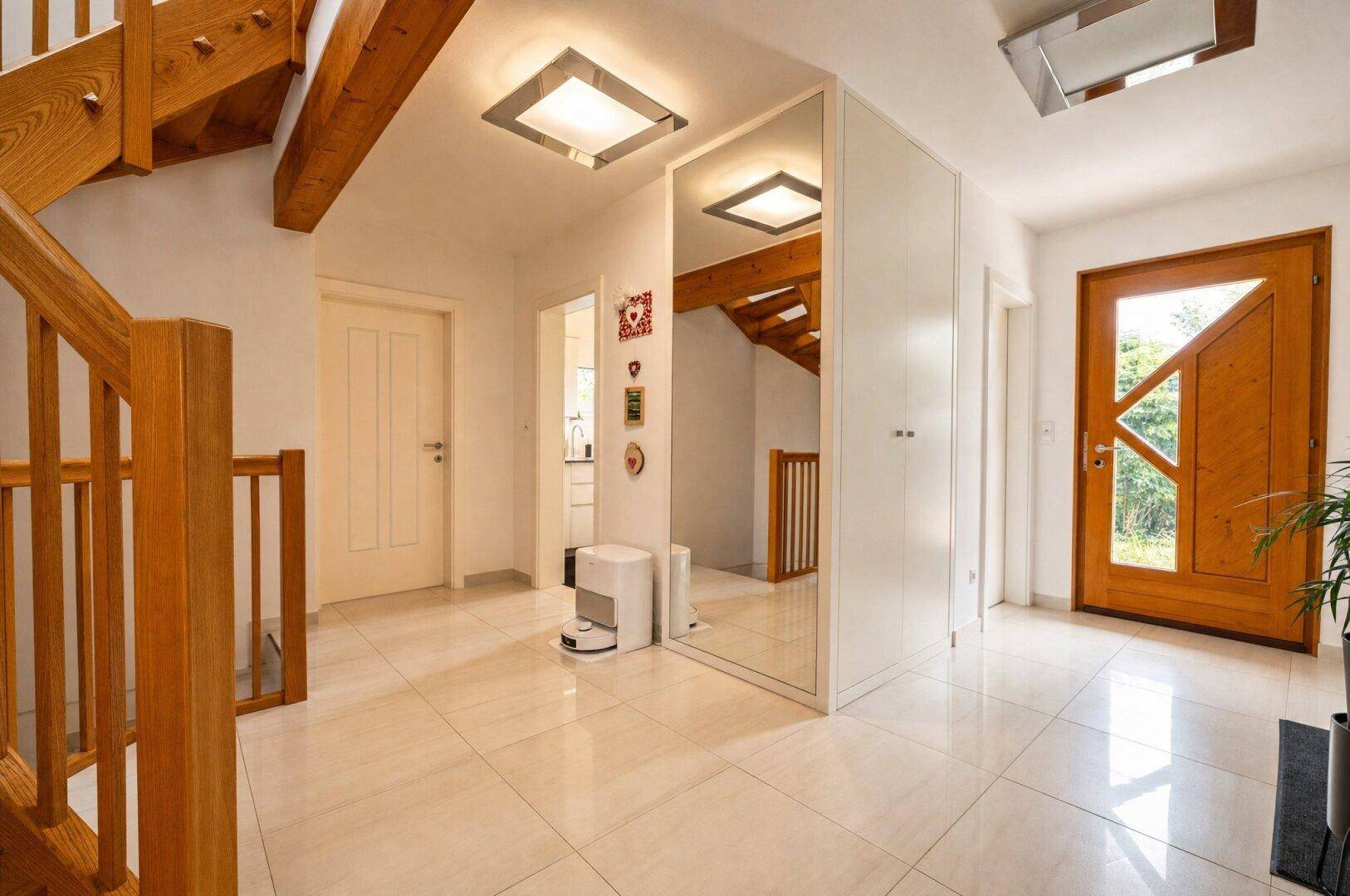 Geräumiger Flur mit hellem Fliesenboden, Holztreppe und großem Spiegel, der den Raum erweitert.