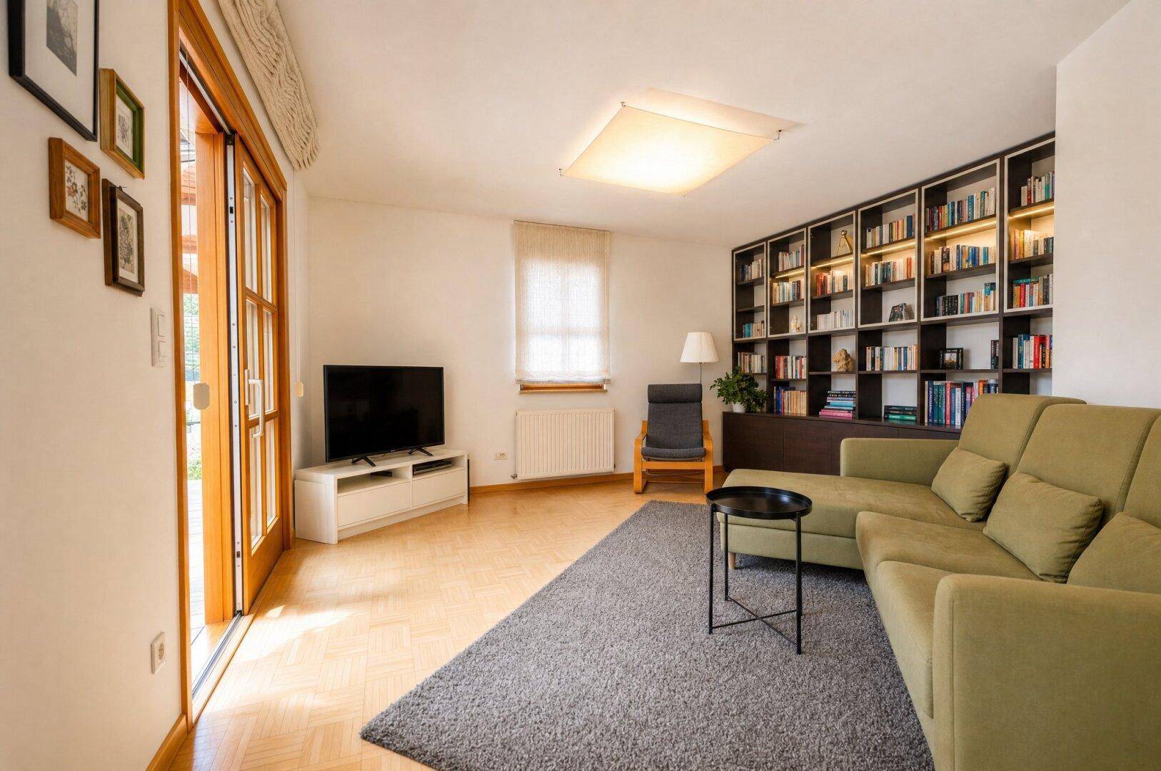Gemütliches Wohnzimmer mit Parkettboden, großem Sofa, Bücherregal und Zugang zur Terrasse.