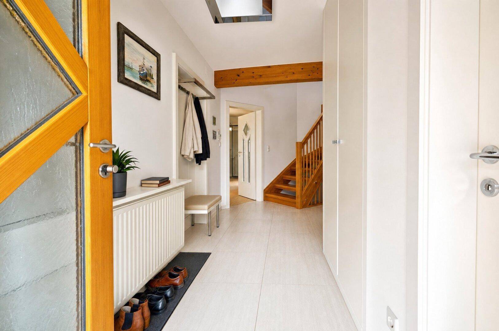 Heller Eingangsbereich mit Fliesenboden, Garderobe und Blick auf die Holztreppe ins Obergeschoss.