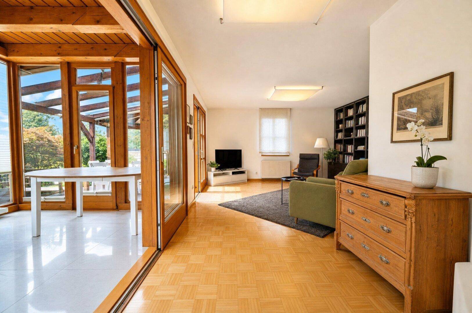 Helles Wohnzimmer mit Parkettboden, Bücherregal und direktem Zugang zum angrenzenden Wintergarten.