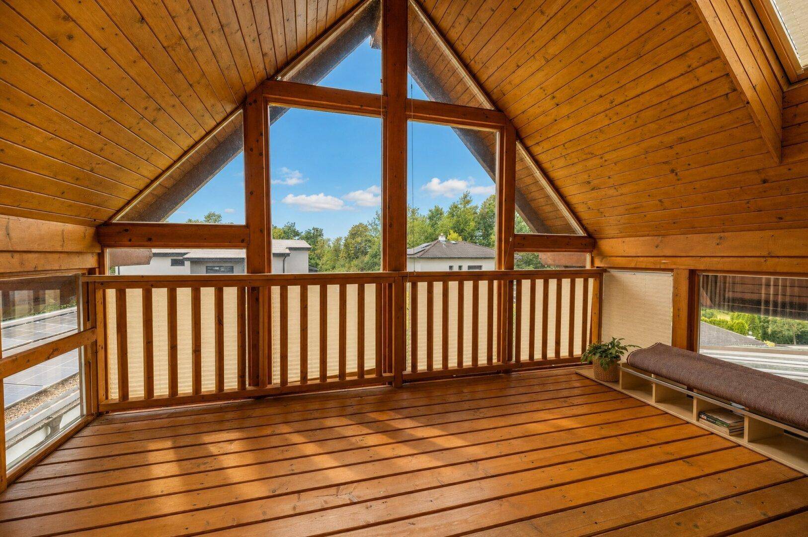Offener Raum im Dachgeschoss mit Holzboden, großen Giebelfenstern und Holzbalkendecke.