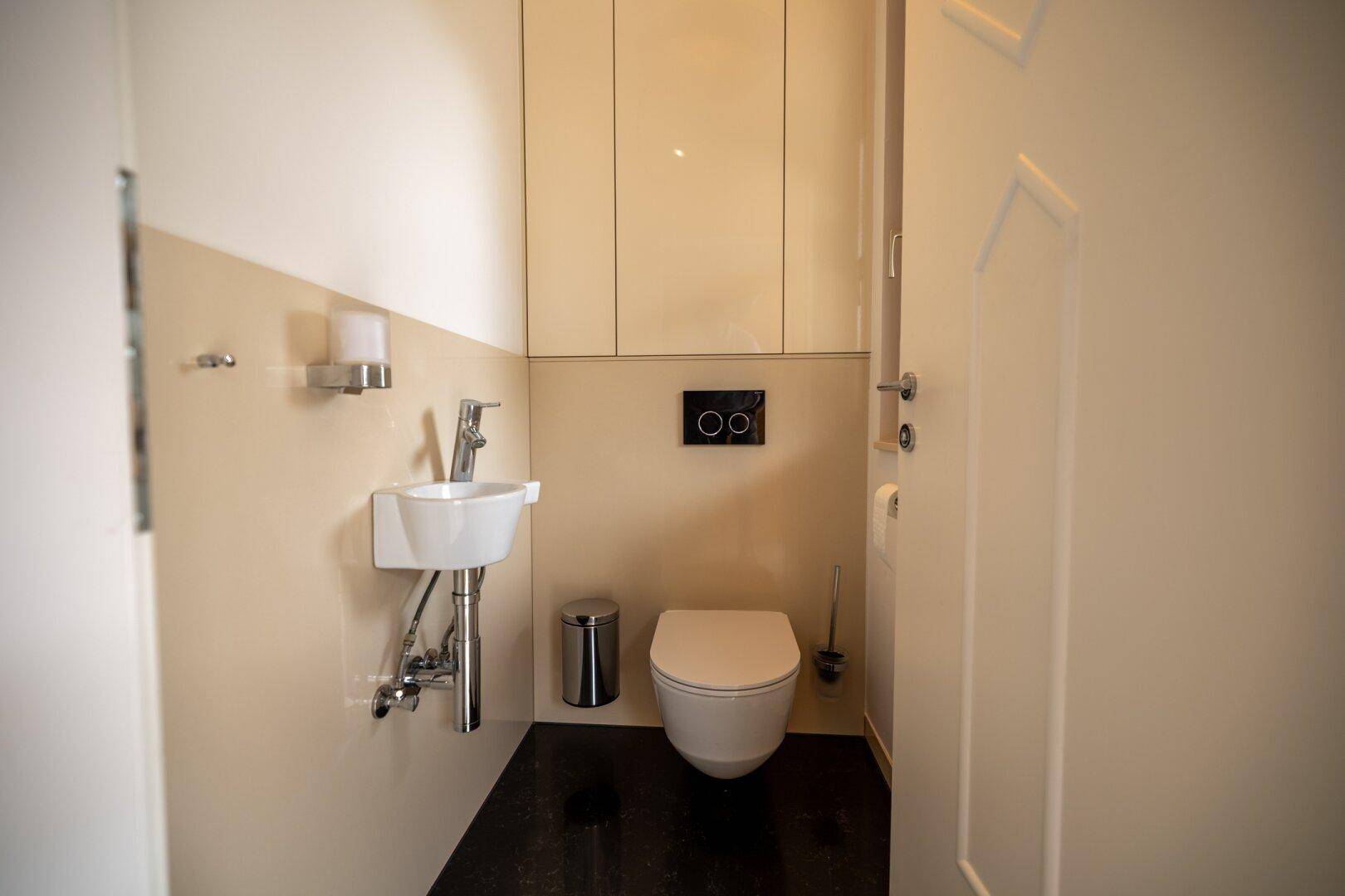 Kleines Gäste-WC mit modernem Wand-WC, Handwaschbecken und Einbauschränken.