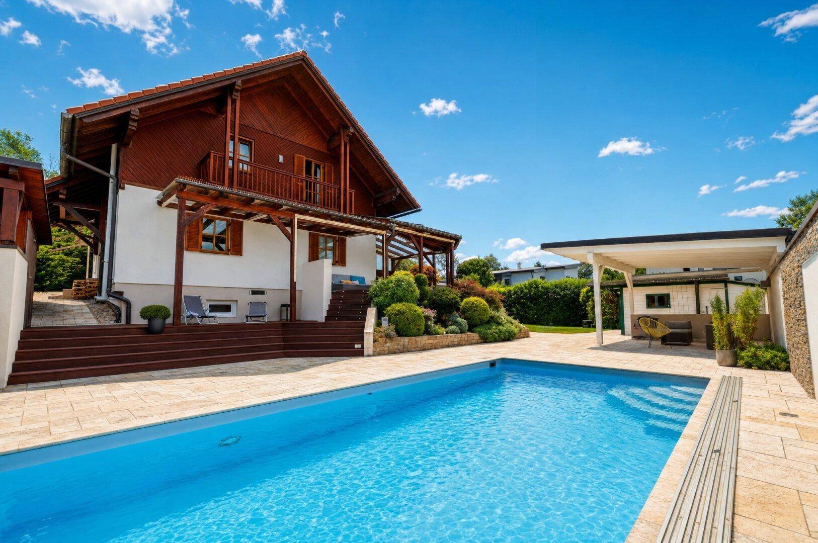 Attraktives Haus mit großem Poolbereich und sonniger Terrasse unter blauem Himmel.