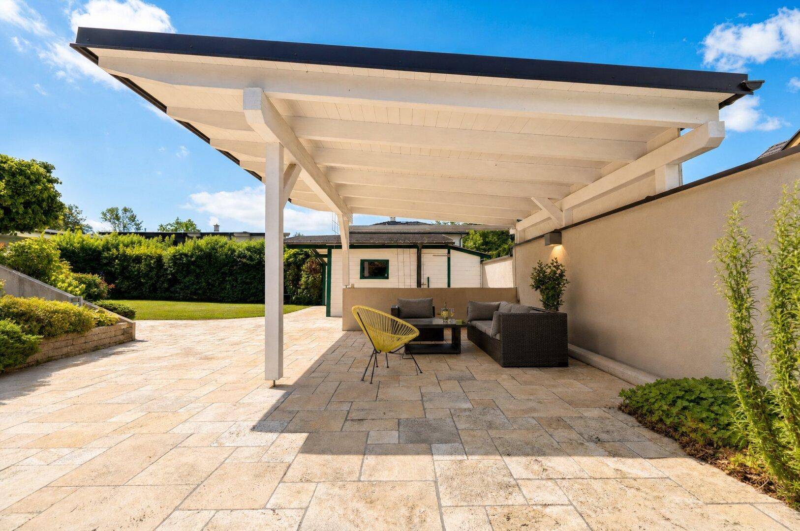 Gemütliche überdachte Terrasse mit modernen Lounge-Möbeln und hellem Steinplattenboden.