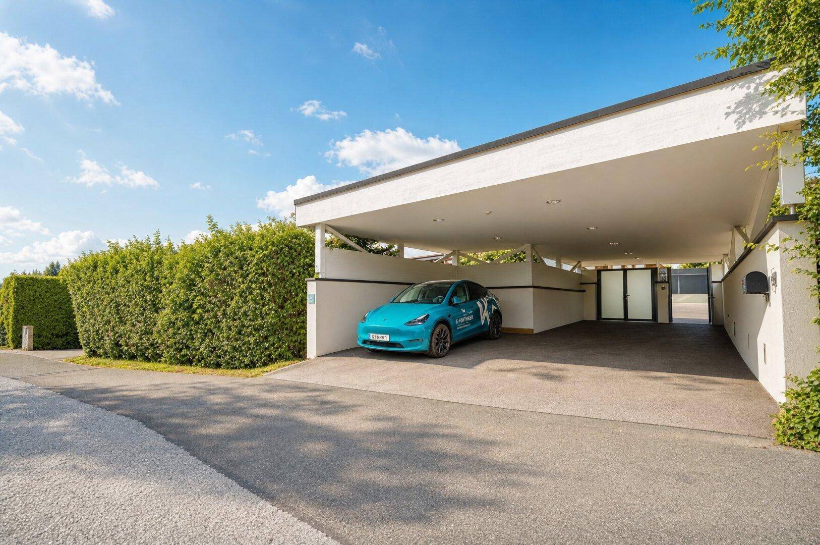 Moderner Carport bietet geschützten Stellplatz für ein Fahrzeug, umgeben von einer hohen Hecke.
