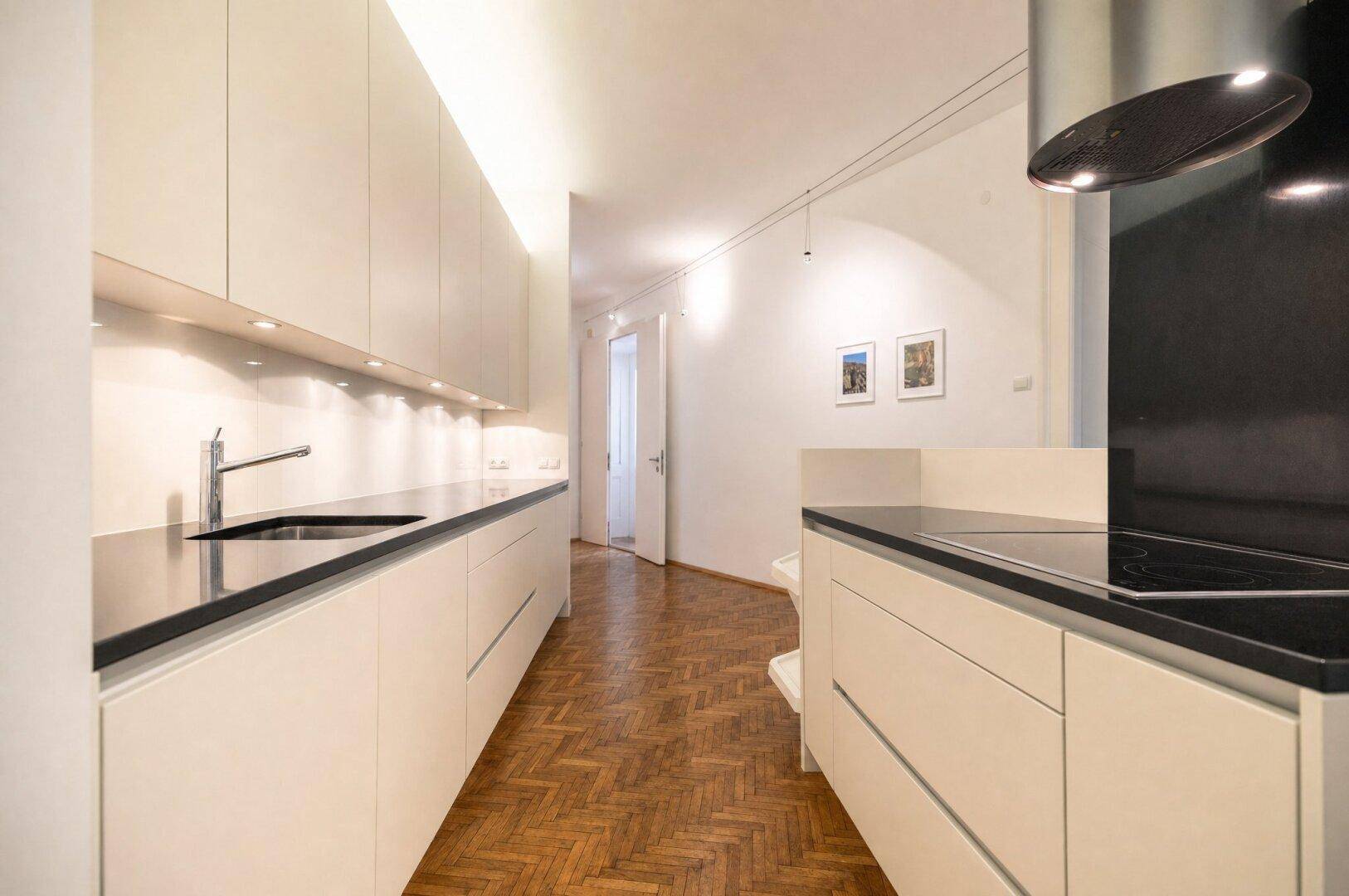 Schmale, moderne Küche mit weißen Fronten, dunkler Arbeitsplatte und Induktionskochfeld.