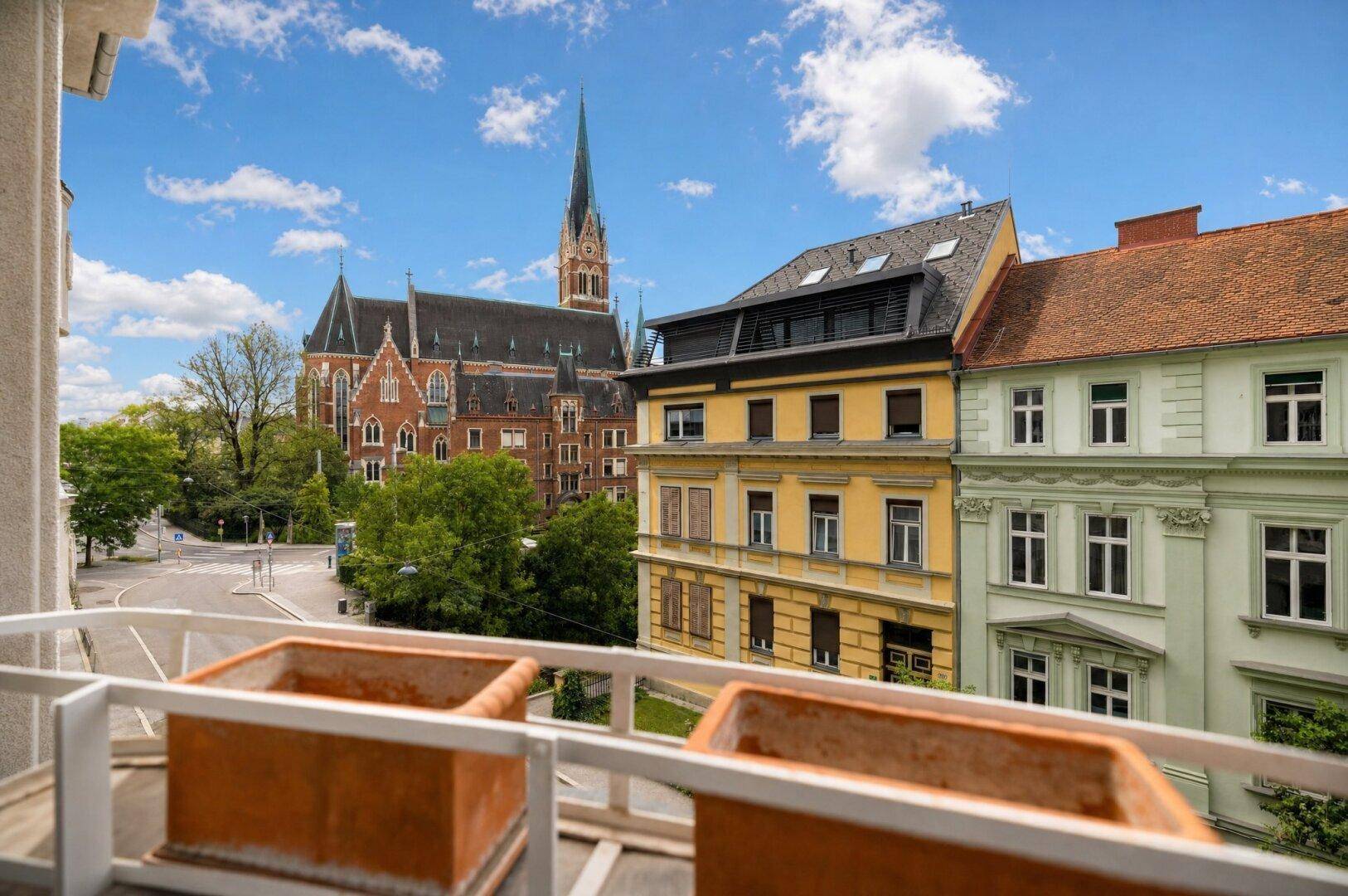Balkon mit Stadtblick und historischer Kirche im Hintergrund unter blauem Himmel.