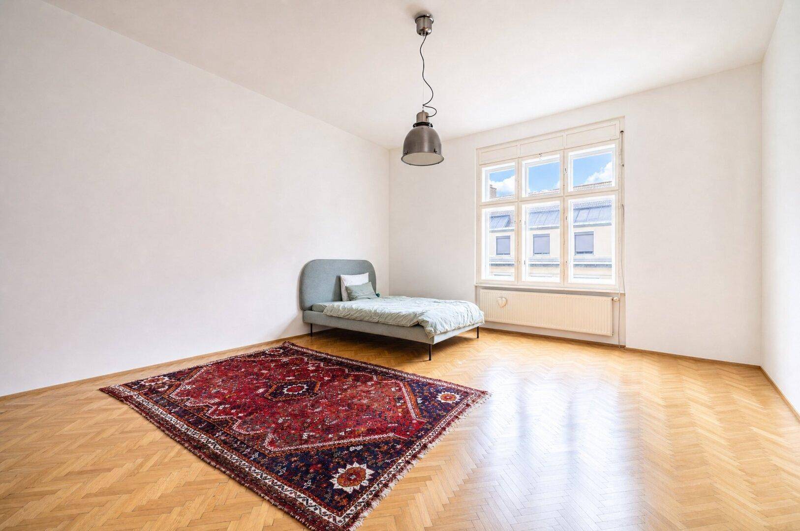 Ruhiges Schlafzimmer mit Fischgrätparkett, großem Fenster und orientalischem Teppich.