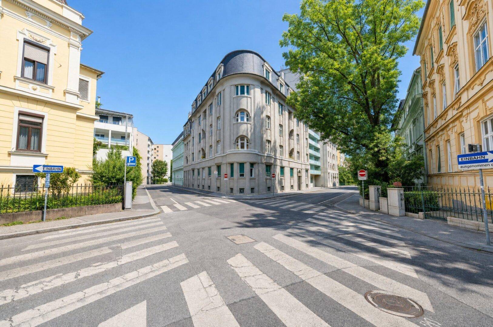 Historisches Eckgebäude an einer belebten Straße mit Zebrastreifen und Bäumen.