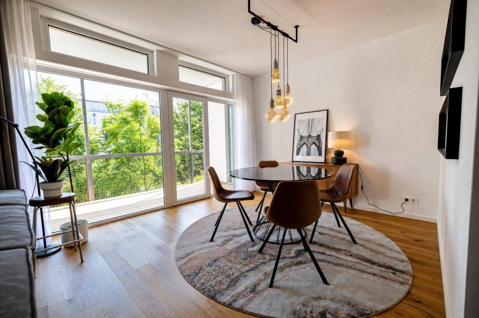 Moderner Essbereich mit rundem Teppich, elegantem Esstisch und Zugang zu einem Balkon mit Grünblick.