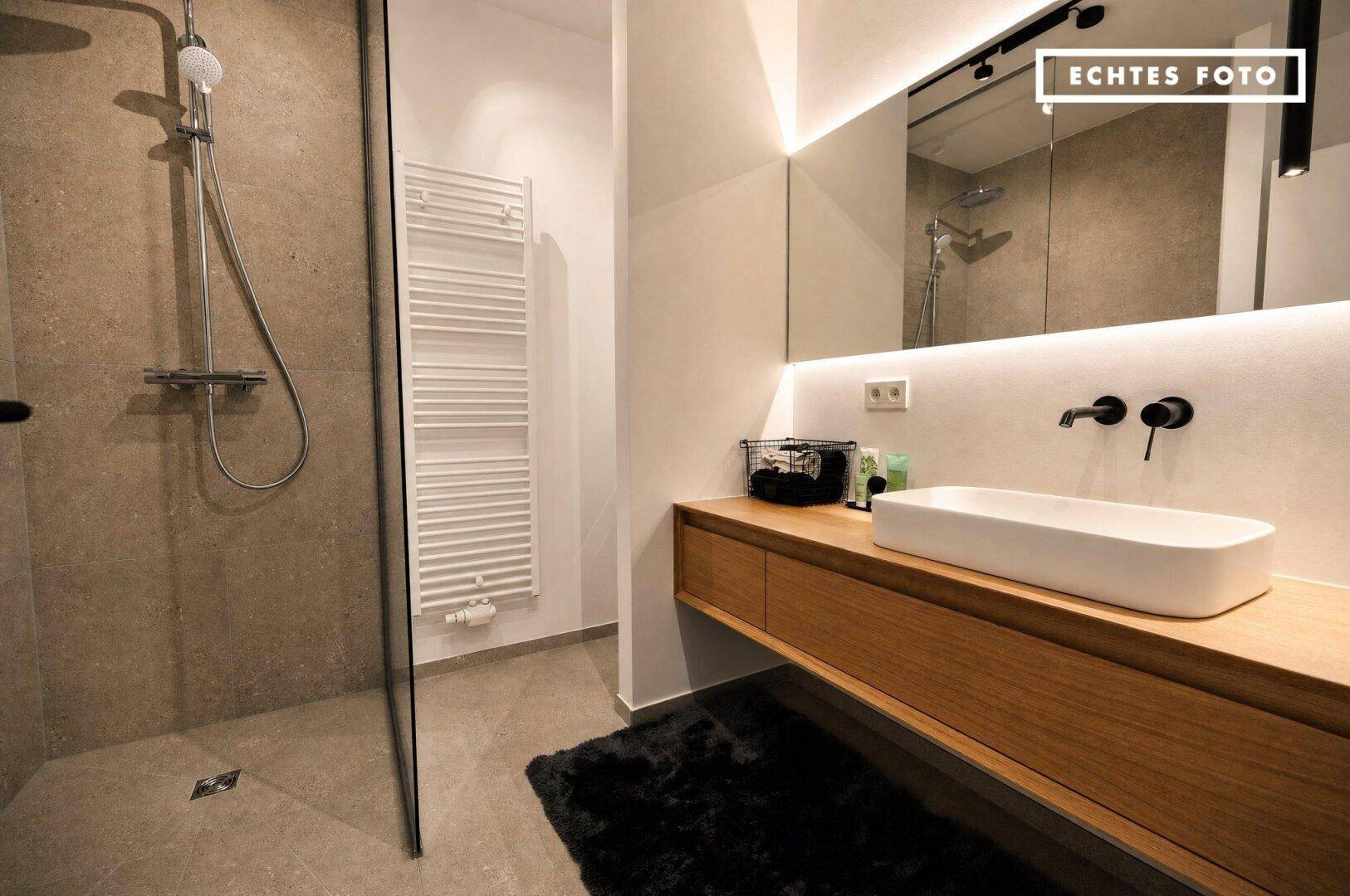 Modernes Badezimmer mit begehbarer Dusche, Holzwaschtisch und beheiztem Handtuchhalter an der Wand.