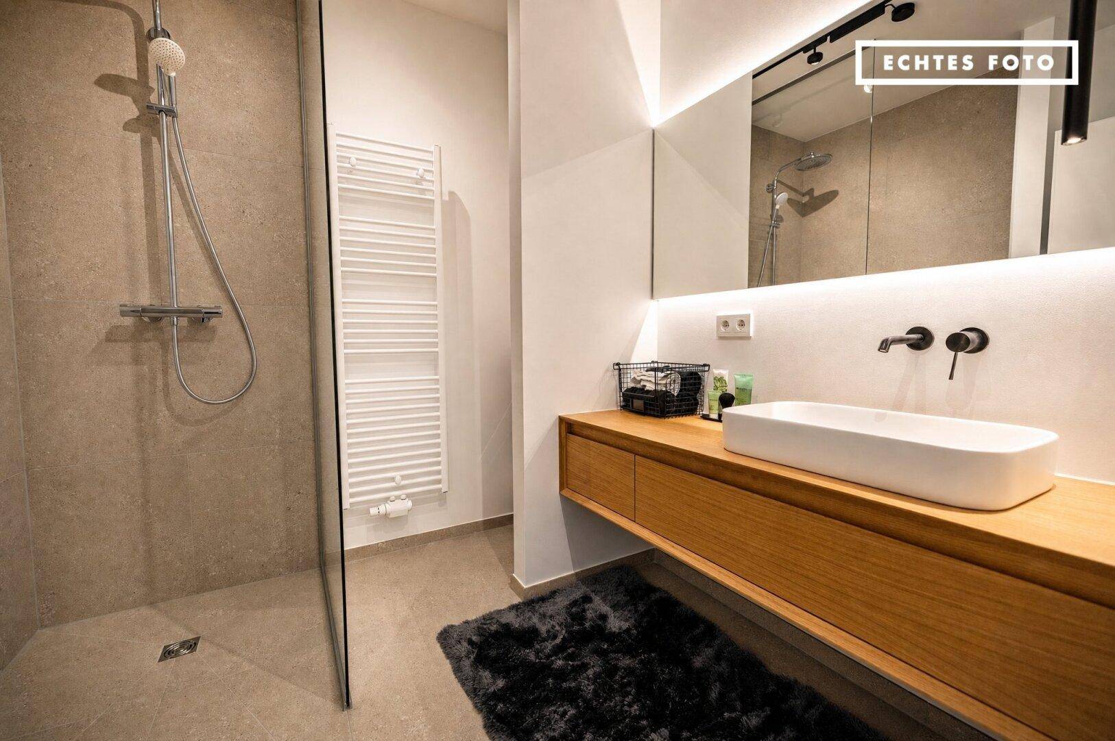 Modernes Badezimmer mit begehbarer Dusche, Holzwaschtisch und beheiztem Handtuchhalter an der Wand.