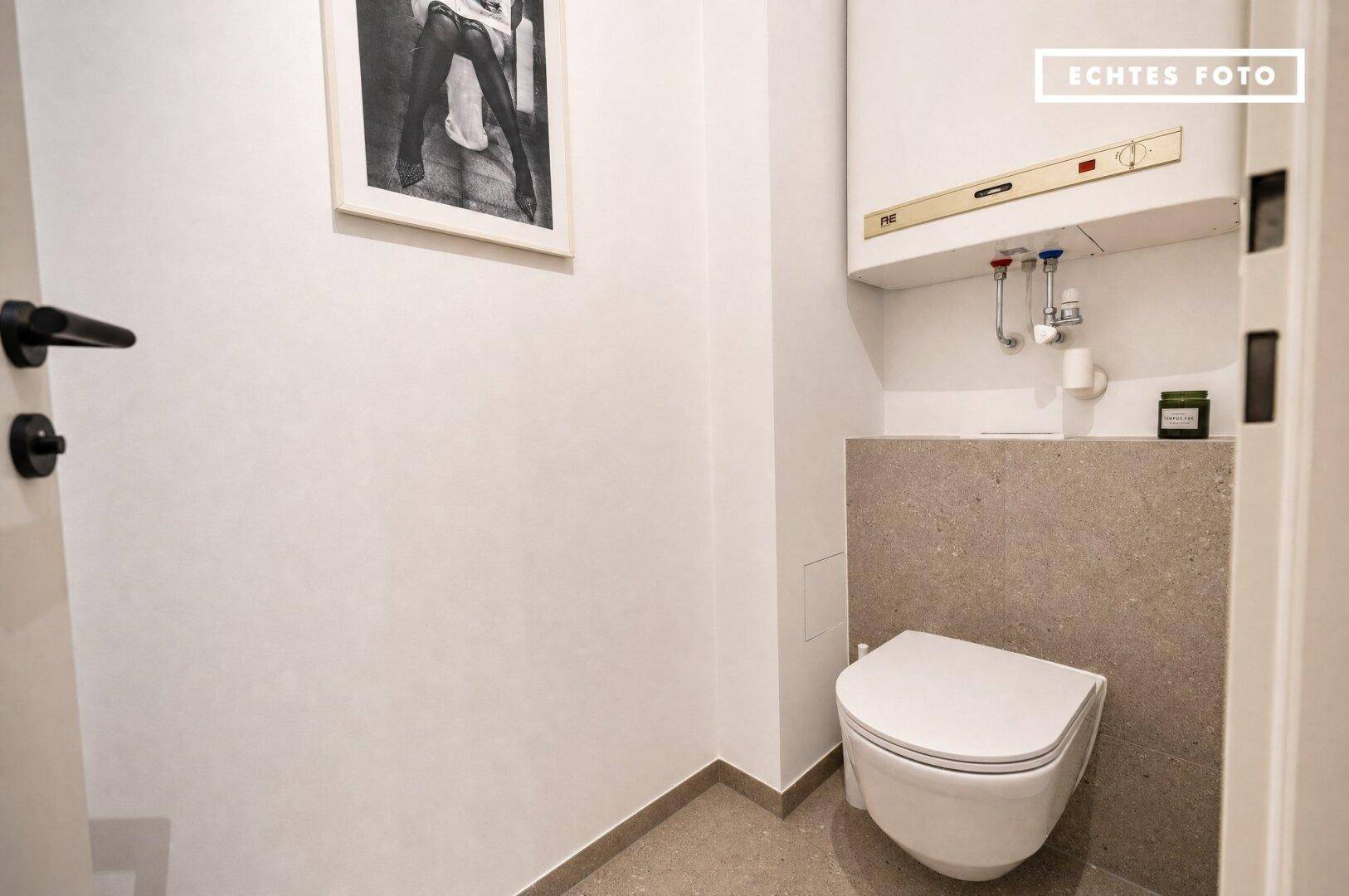Separates WC mit wandhängender Toilette und kleinem Warmwasserboiler, funktional und platzsparend.