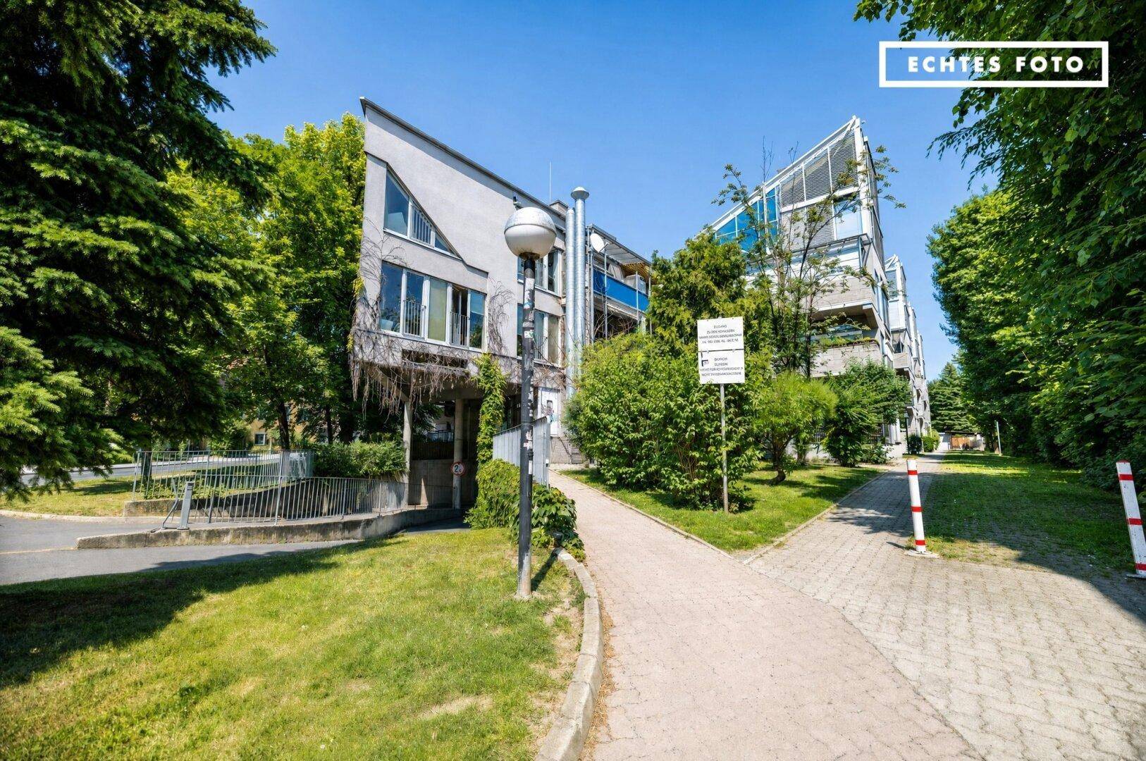 Moderne Wohnanlage mit viel Grün, gepflasterten Wegen und Zufahrt zur Tiefgarage.