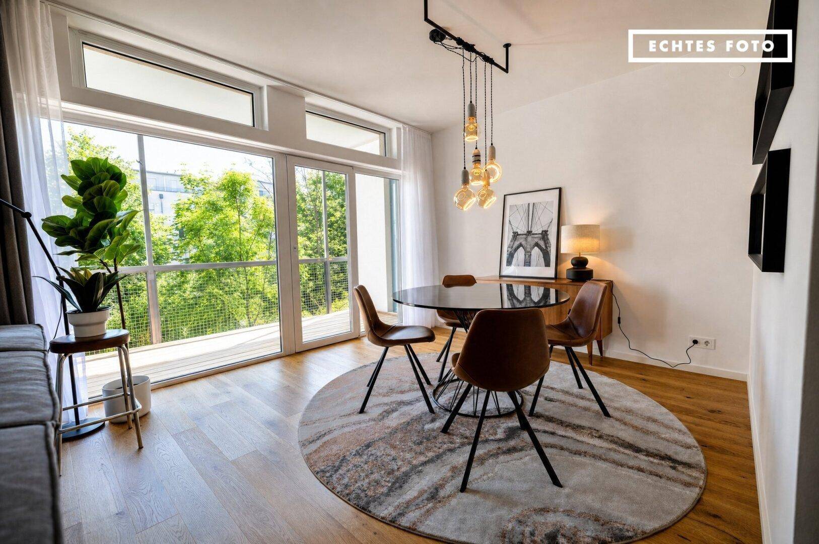 Heller Essbereich mit modernem runden Tisch, braunen Stühlen und Zugang zum Balkon mit viel Grün.
