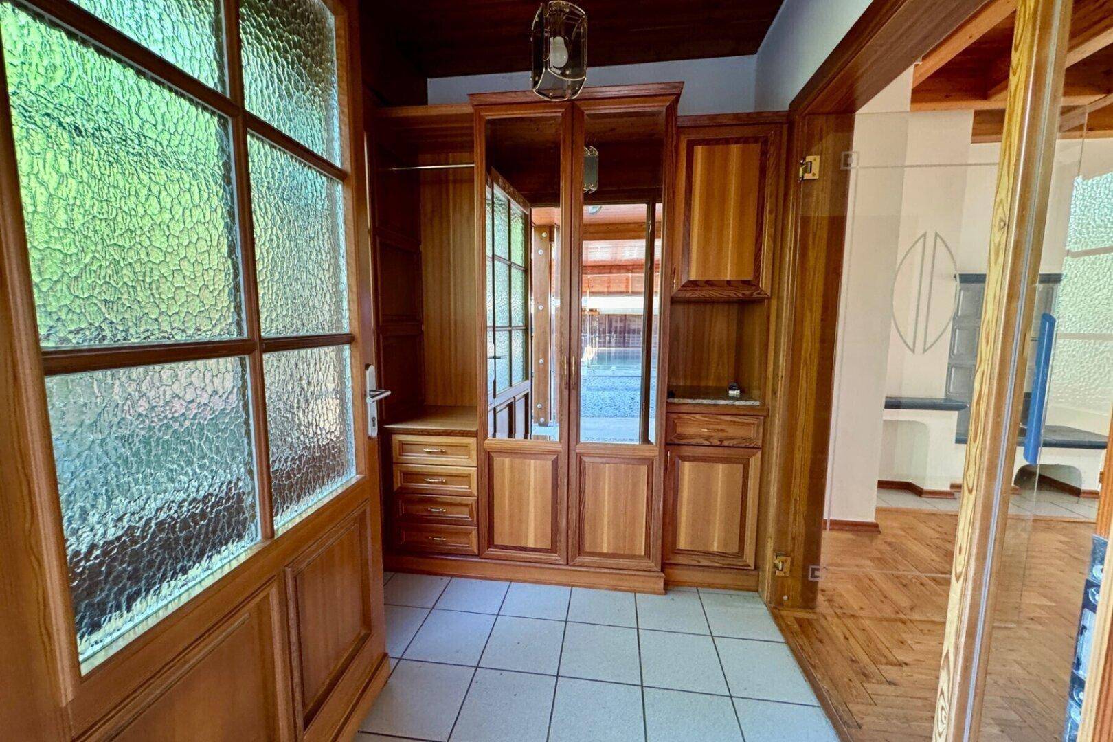 Eingangsbereich mit Fliesenboden und einem großen Holzschrank mit Spiegeltüren.