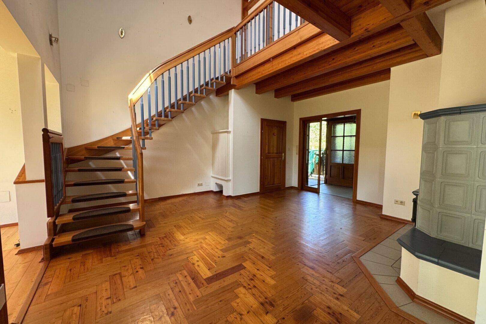 Heller Wohnbereich mit eleganter Holztreppe, Fischgrätparkett und traditionellem Kachelofen.