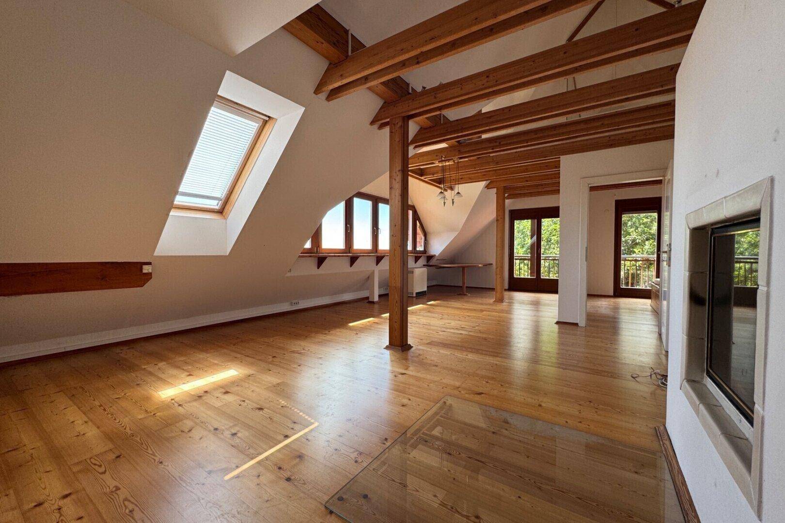 Offener Wohnbereich im Dachgeschoss mit Holzbalken, Dielenboden und großen Fenstern.