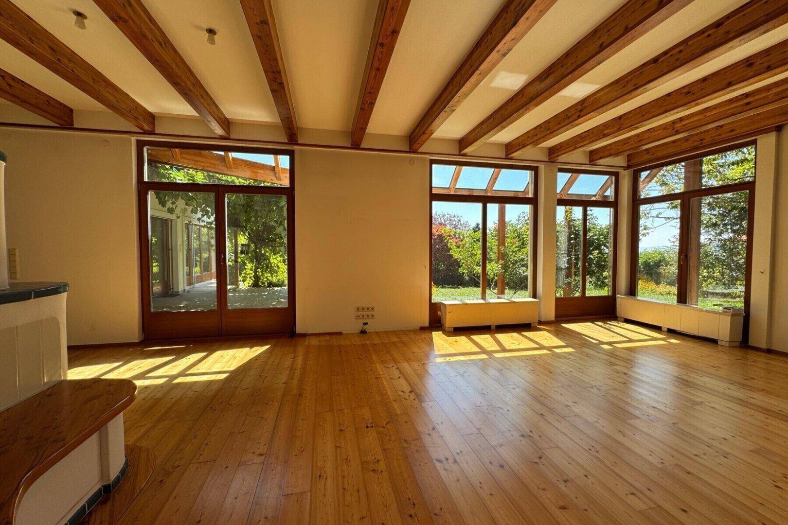 Lichtdurchflutetes Wohnzimmer mit Holzdielenboden und großen Fenstern, die viel Tageslicht hereinlassen.