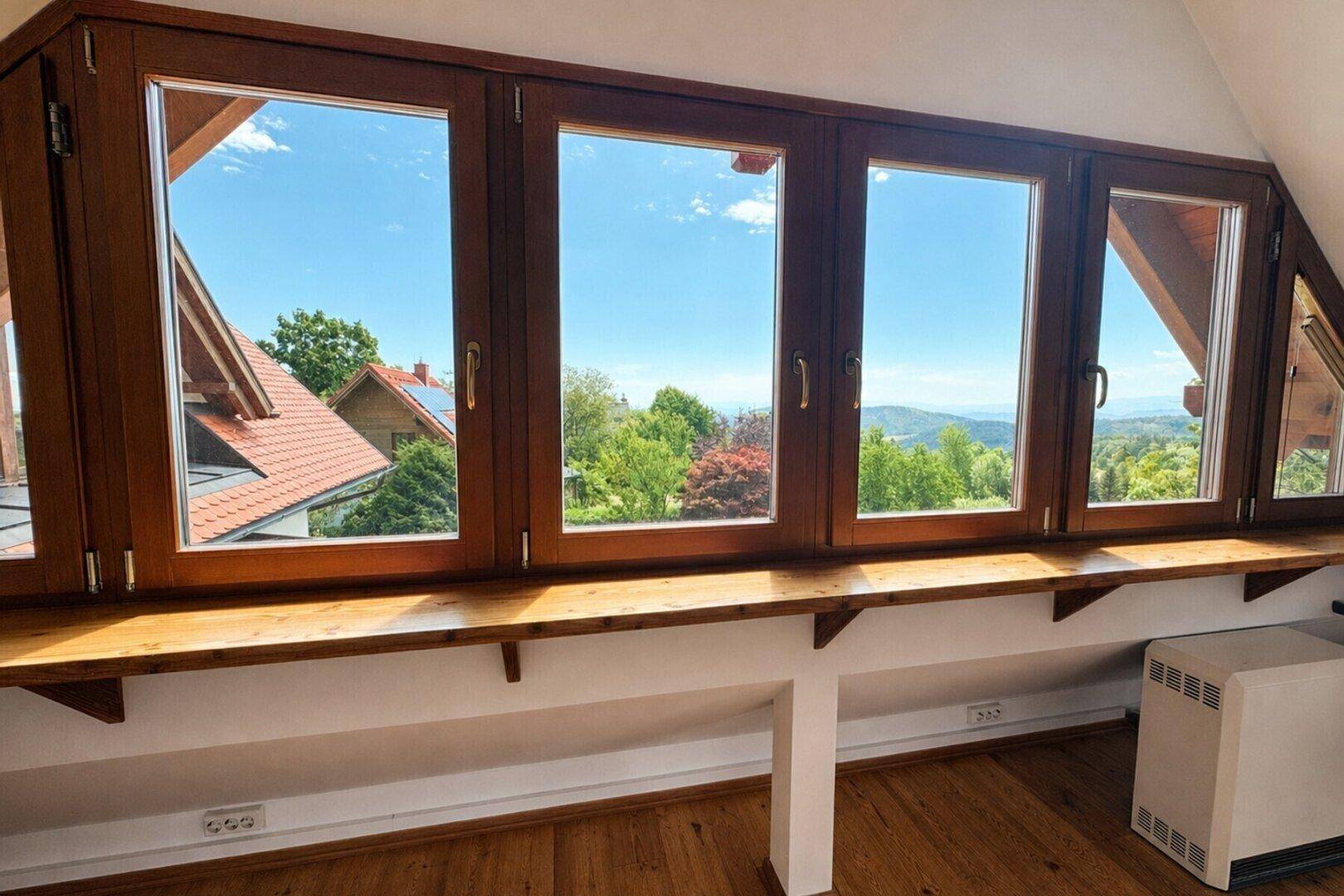 Raum mit großen Holzfenstern bietet einen weiten Blick auf die grüne Landschaft und Berge.