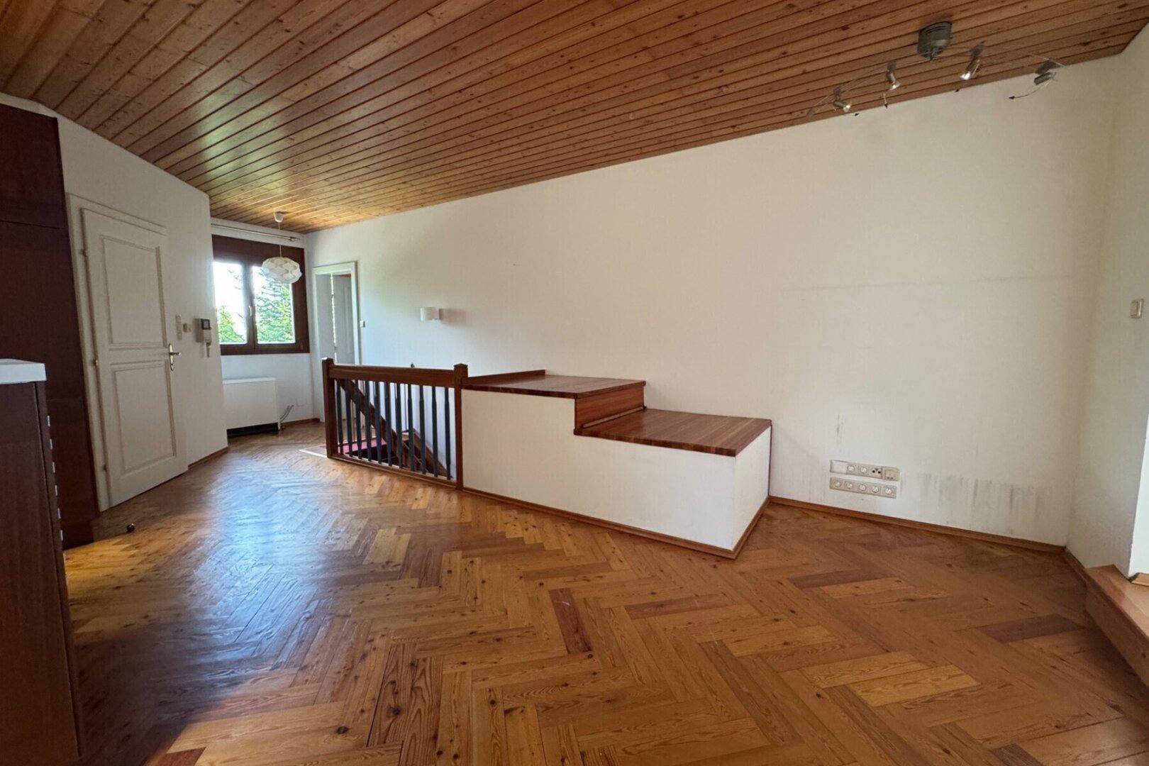 Offener Bereich mit Holzdecke, Fischgrätparkett und Treppenabgang.