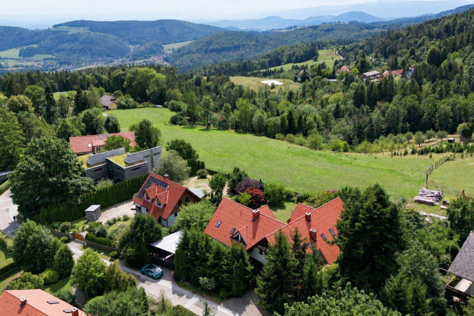 Weitläufige Luftaufnahme der ländlichen Umgebung mit Häusern, Wäldern und grünen Wiesen.