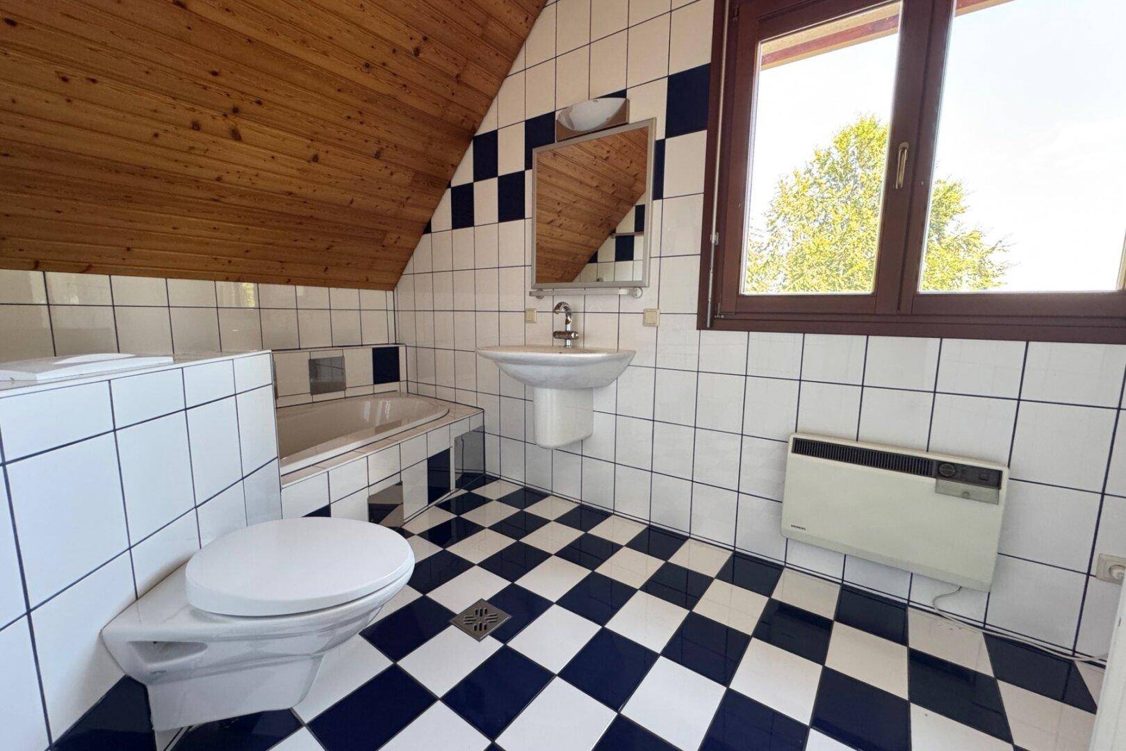 Badezimmer im Dachgeschoss mit blau-weiß karierten Fliesen, Badewanne und Fenster.
