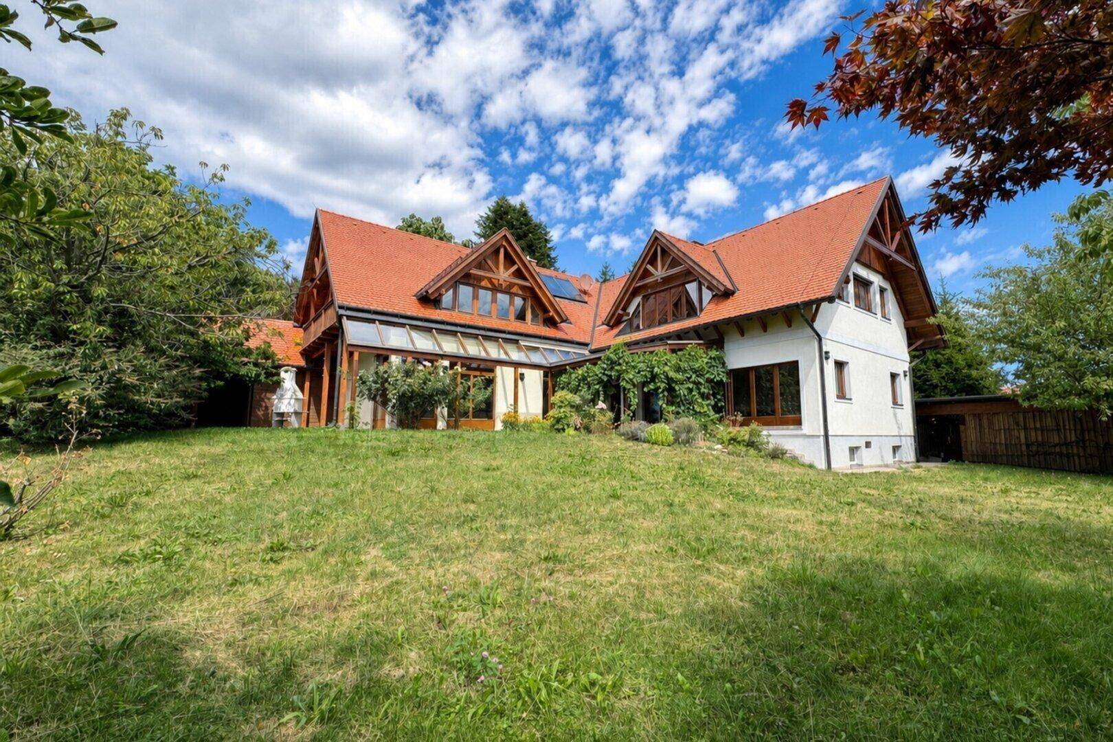 Charmantes Haus mit rotem Ziegeldach und weitläufigem Garten unter blauem Himmel.