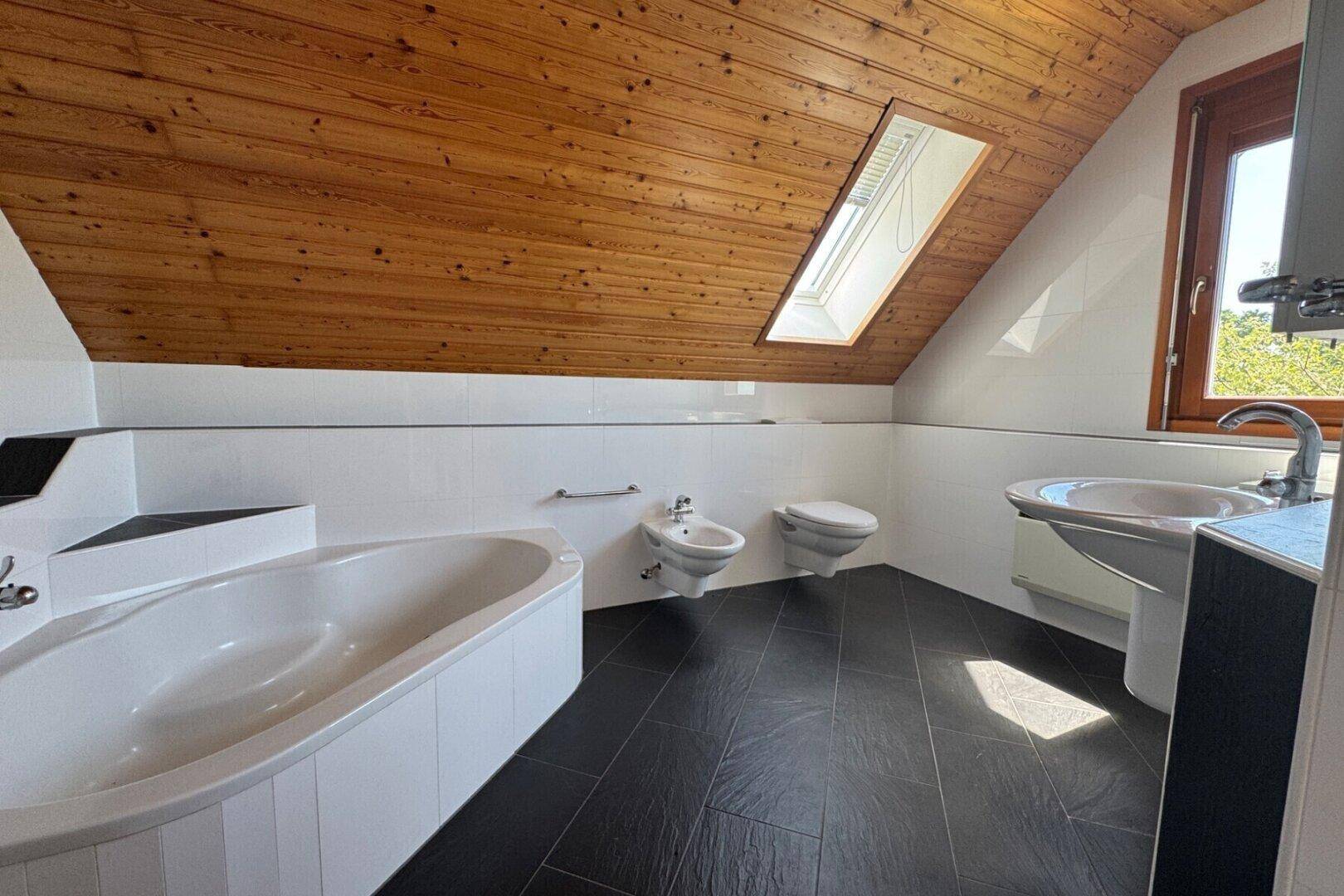 Modernes Badezimmer im Dachgeschoss mit Badewanne, Bidet, WC und Dachfenster.