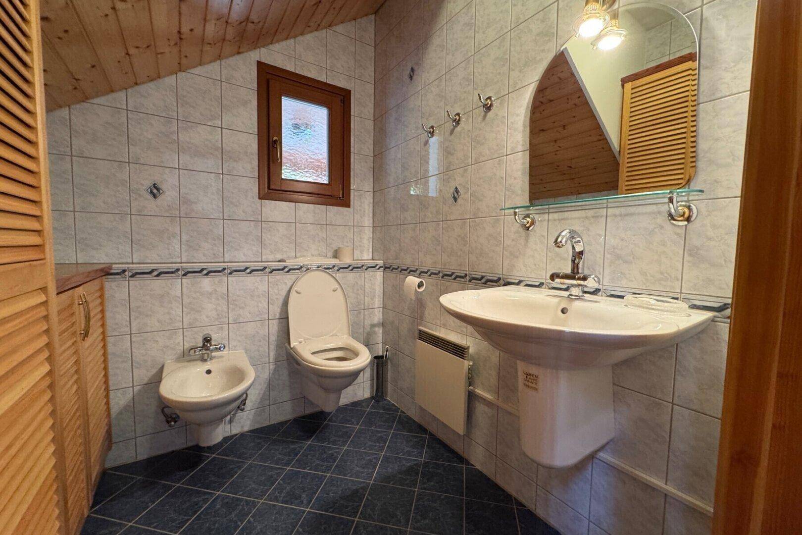 Badezimmer mit Dachschräge, Fliesenboden, Waschbecken, WC und Bidet.