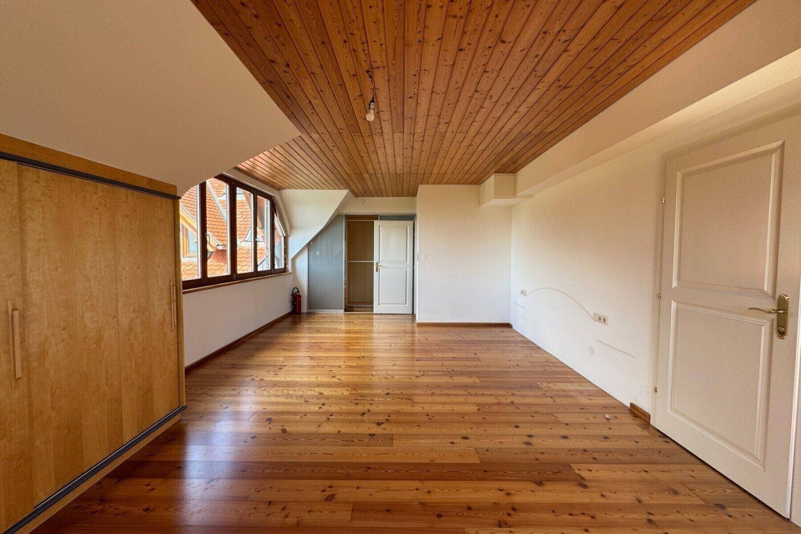 Geräumiges Zimmer im Dachgeschoss mit Holzdecke, Dielenboden und Einbauschrank.