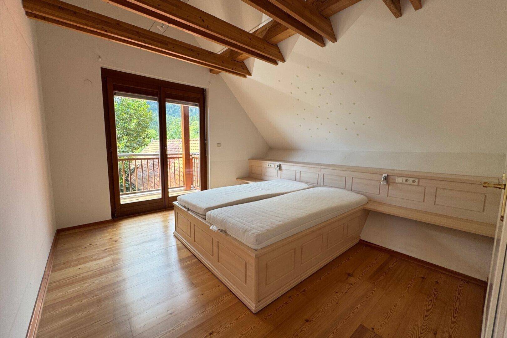 Helles Schlafzimmer im Dachgeschoss mit Holzbalken, Parkettboden und Balkonzugang.
