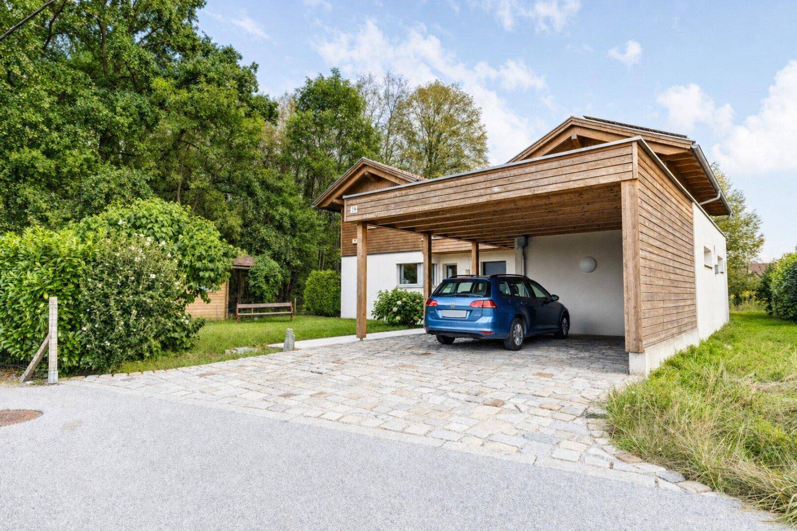 Modernes Haus mit Holzfassade, Carport und gepflasterter Einfahrt im Grünen.