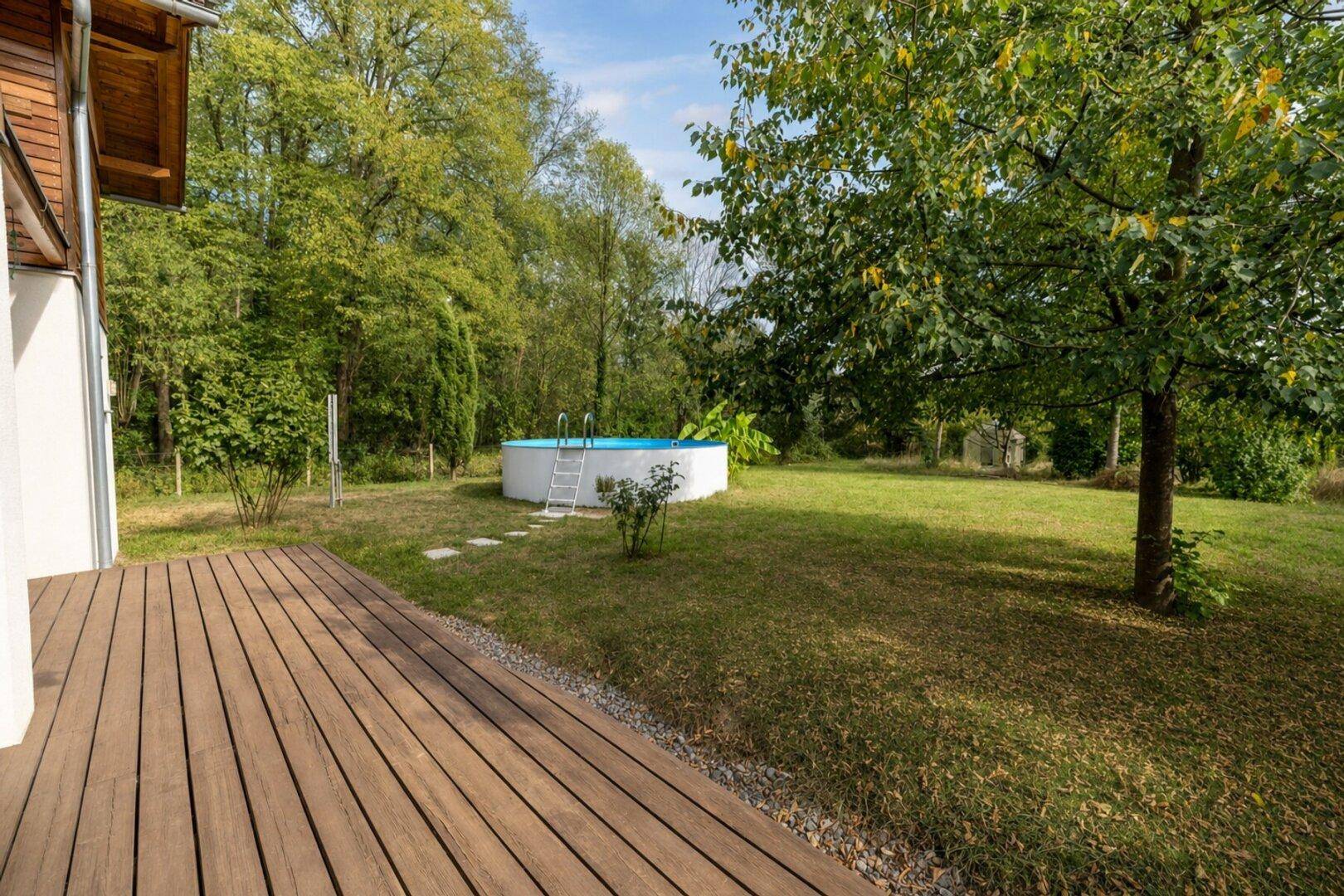 Großer Garten mit Holzterrasse und einem oberirdischen Pool, umgeben von Bäumen.