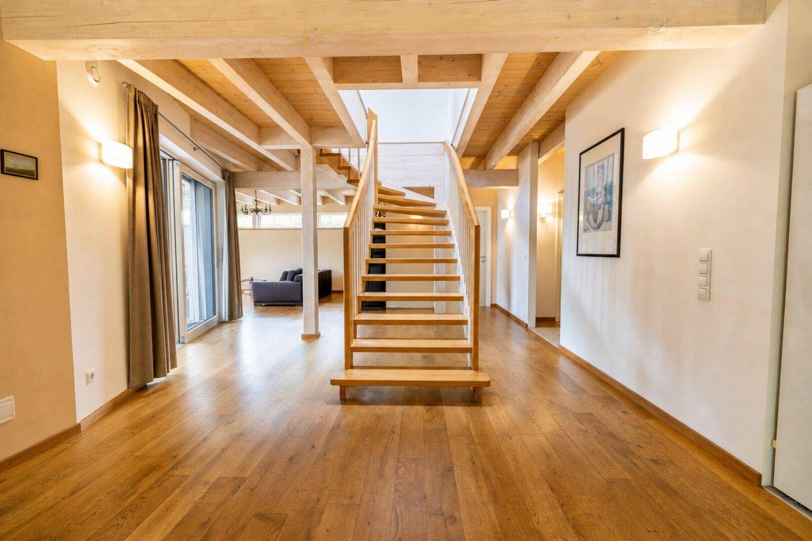 Heller Eingangsbereich mit offener Holztreppe, Holzbalkendecke und Parkettboden.