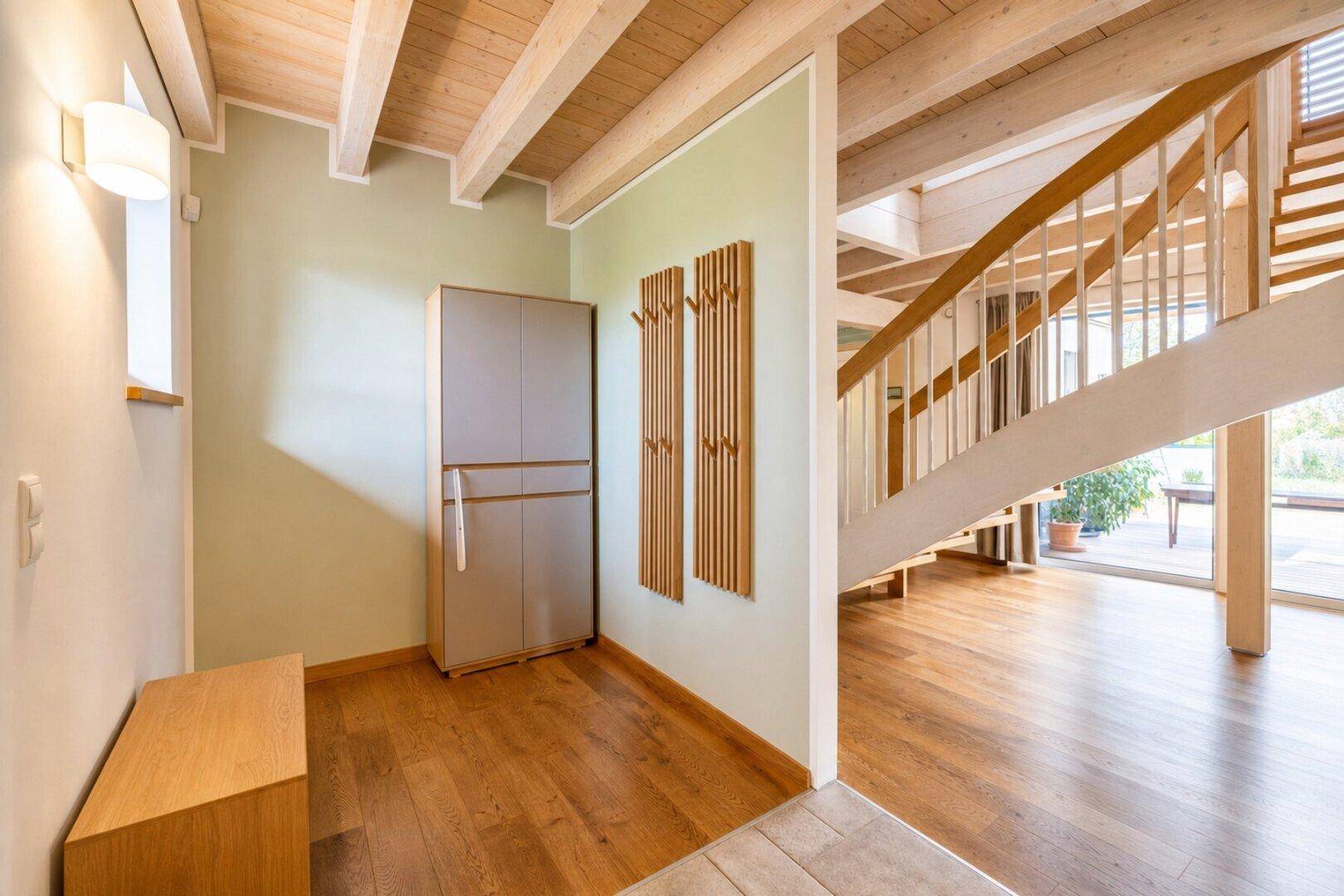 Heller Flur mit Holzbalkendecke, Garderobe und offener Treppe zum Obergeschoss.