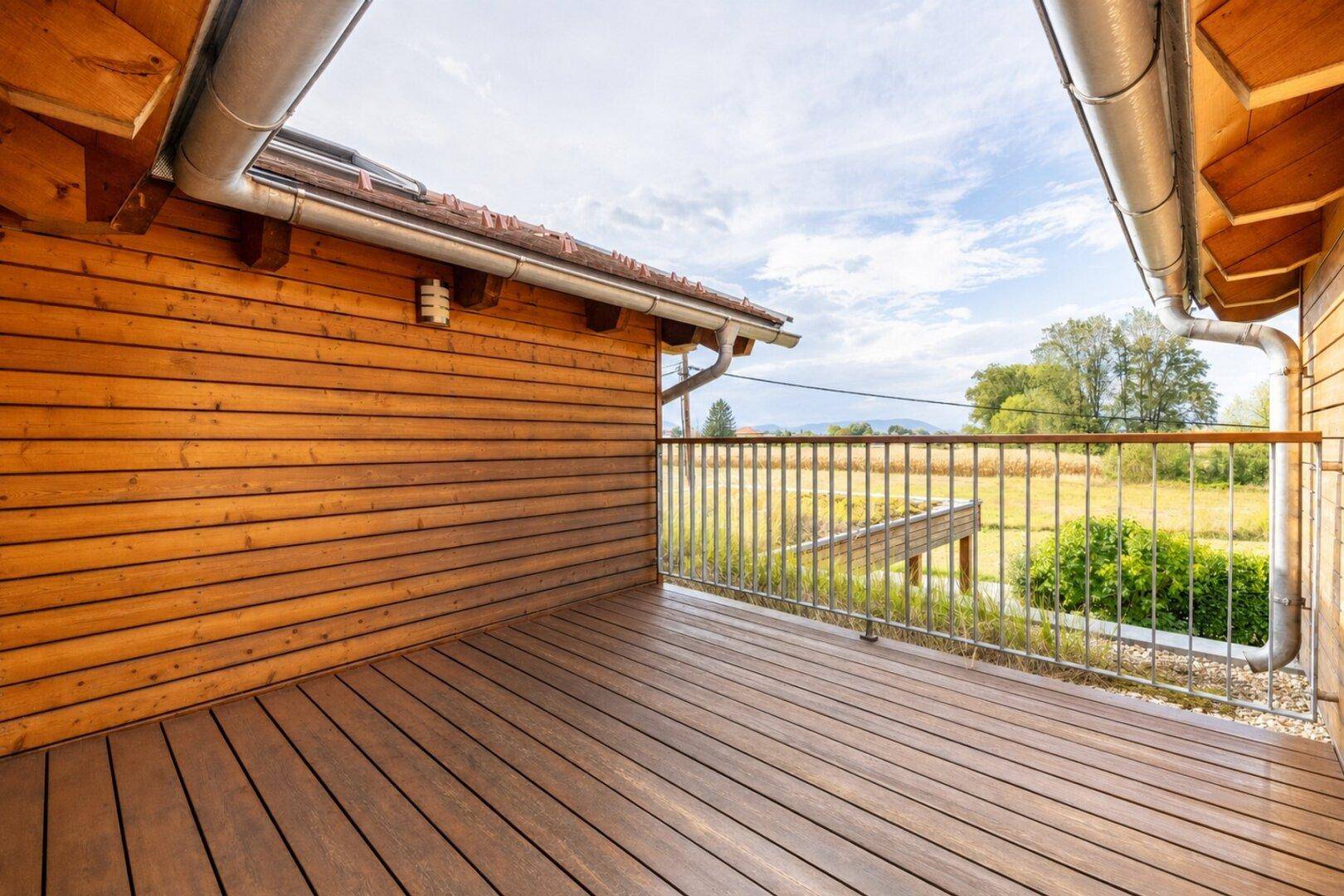 Großer Holzbalkon mit Metallgeländer und weitem Blick über die Landschaft.