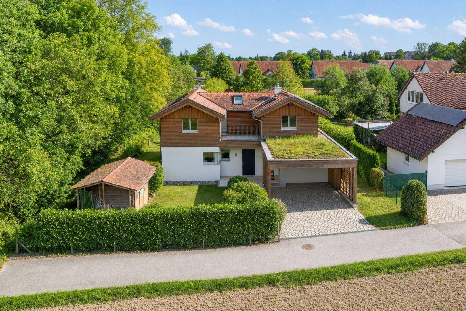 Luftaufnahme eines modernen Einfamilienhauses mit Gründach-Carport und gepflegtem Gartenbereich.
