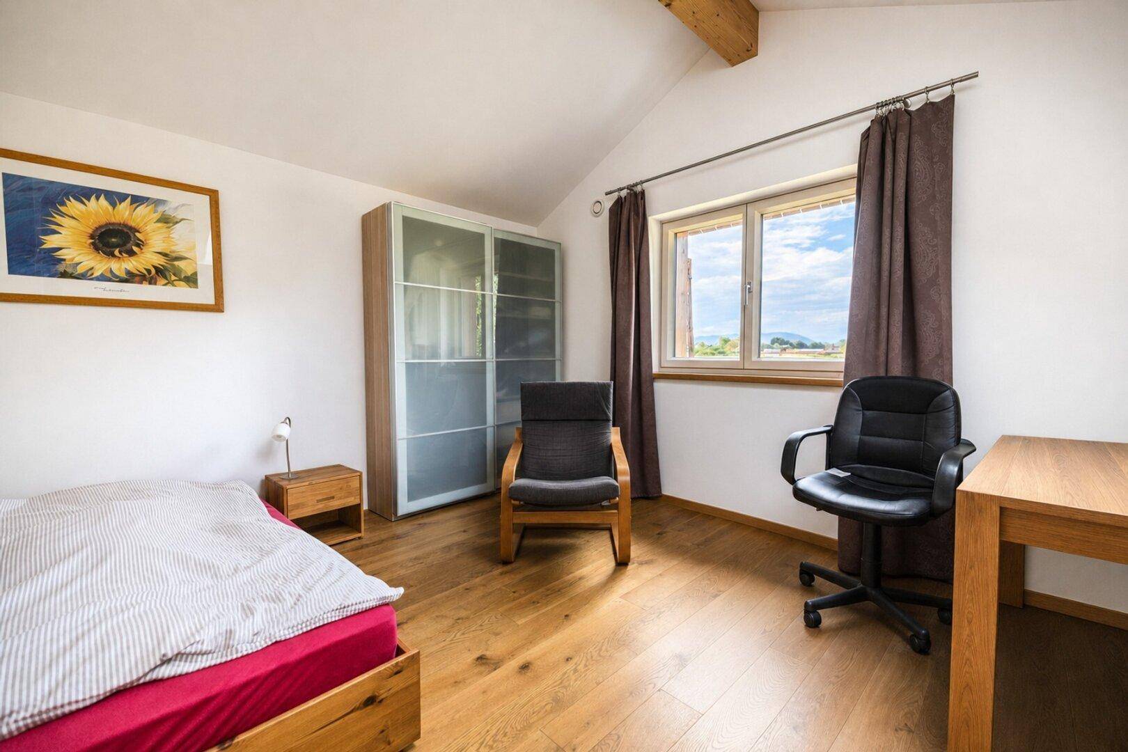 Geräumiges Schlafzimmer mit Schrank, Schreibtisch und Fenster mit Ausblick.